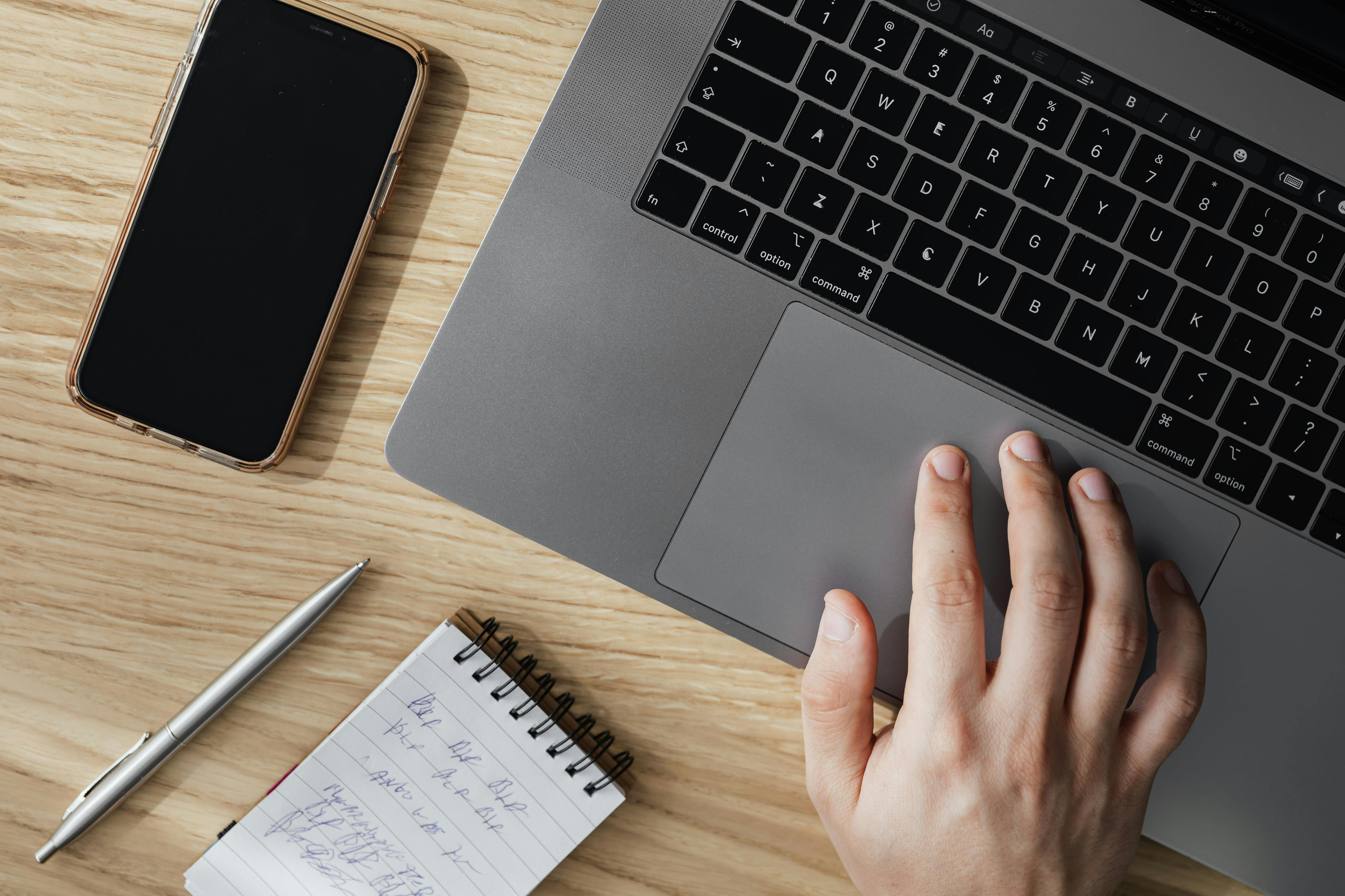 A person uses his laptop while his phone rests beside it | Source: Pexels