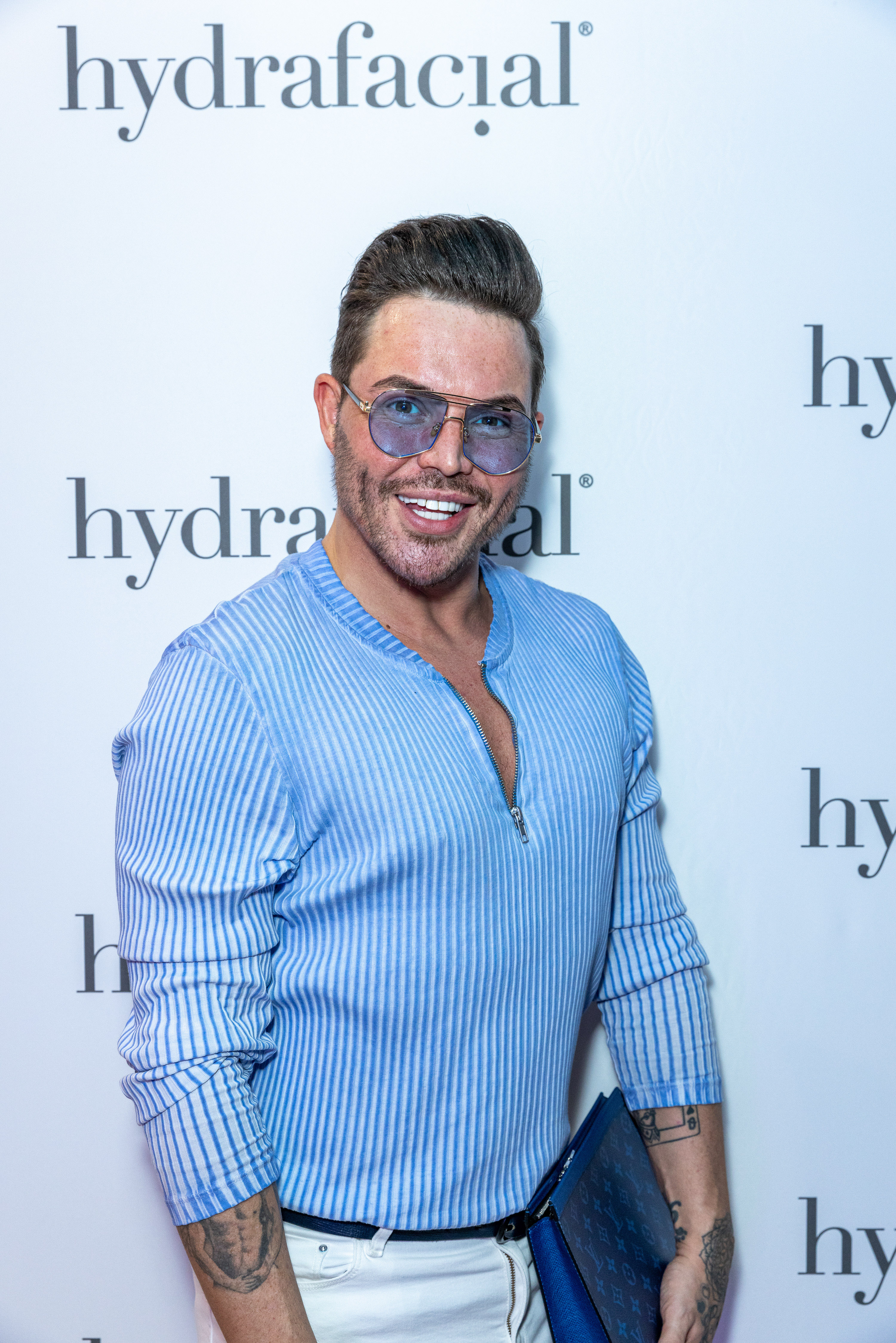 Relaxed and beaming at the Hydrafacial flagship store launch in London in March 2022, Norris wore a powder-blue zip-up shirt, white trousers, and tinted gold-rimmed aviators, a blue monogram clutch tucked under one arm.