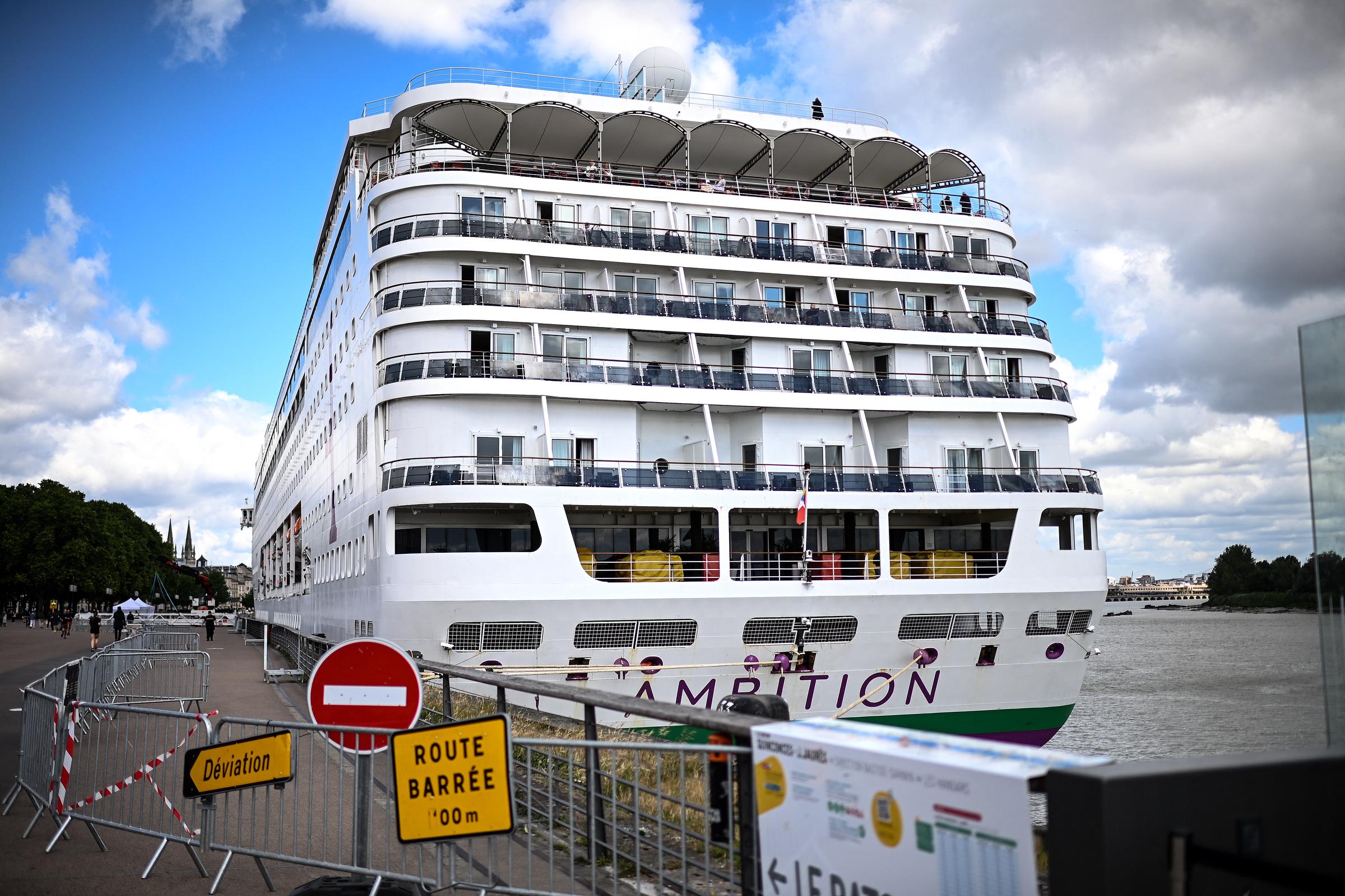 Passengers stand aboard the Bahamas-registered cruise ship Ambition after they were confined following the outbreak of a gastrointestinal illness onboard, at the Bordeaux port in Bordeaux, southwestern France on May 13, 2026. | Source: Getty Images