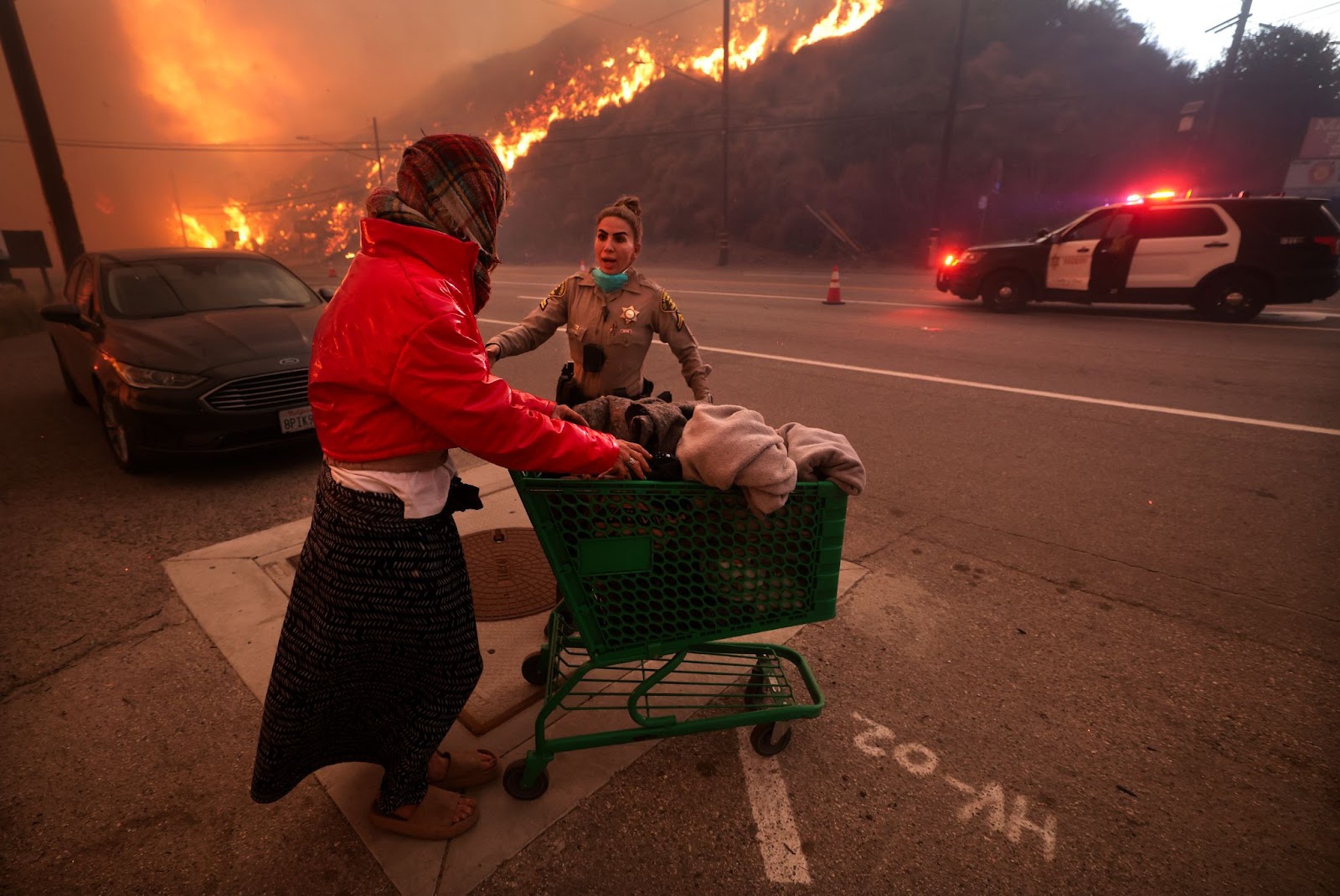 A police officer escorting a homeless woman away from Pacific Coast Highway and Topanga Canyon Boulevard as the Palisades fire raged down the hills in Los Angeles, California, on Tuesday, January 7, 2025. | Source: Getty Images