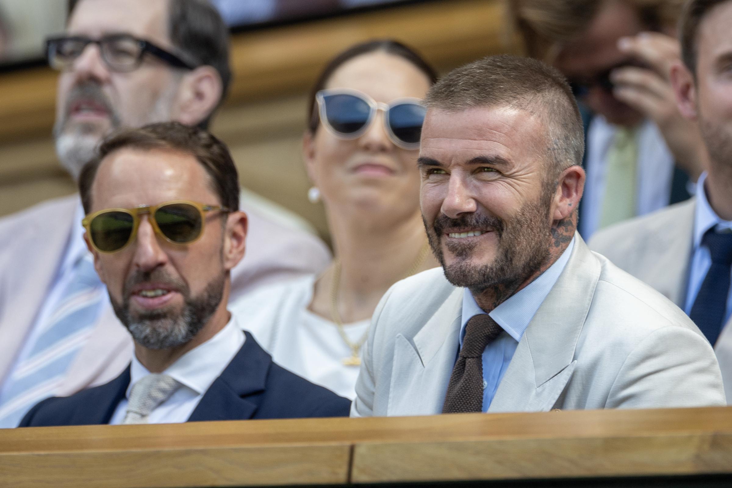 David Beckham sits alongside Gareth Southgate in the Royal Box at Wimbledon. Dressed in a cream suit and blue tie, Beckham smiles as he enjoys the Centre Court action.