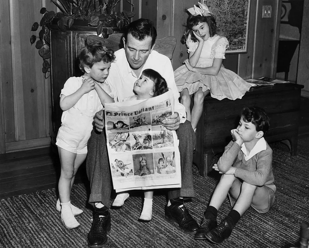 John Wayne liest einen "Prince Valiant"-Comic mit seinen vier Kindern Patrick, Melinda, Toni und Michael in Hollywood, Kalifornien im Jahr 1942. | Quelle: Getty Images