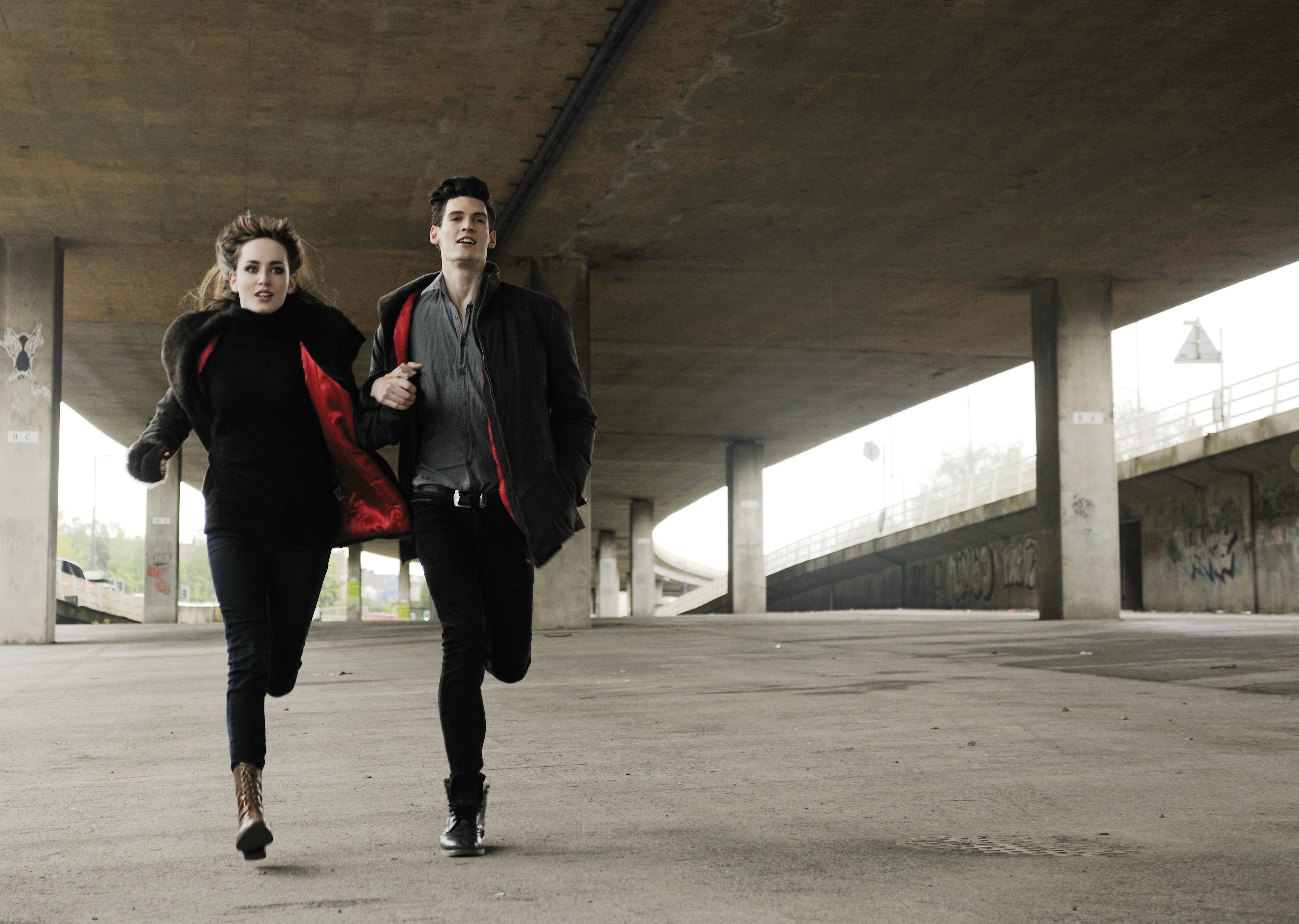 A formerly dressed couple running hand-in-hand under a bridge | Source: Pexels