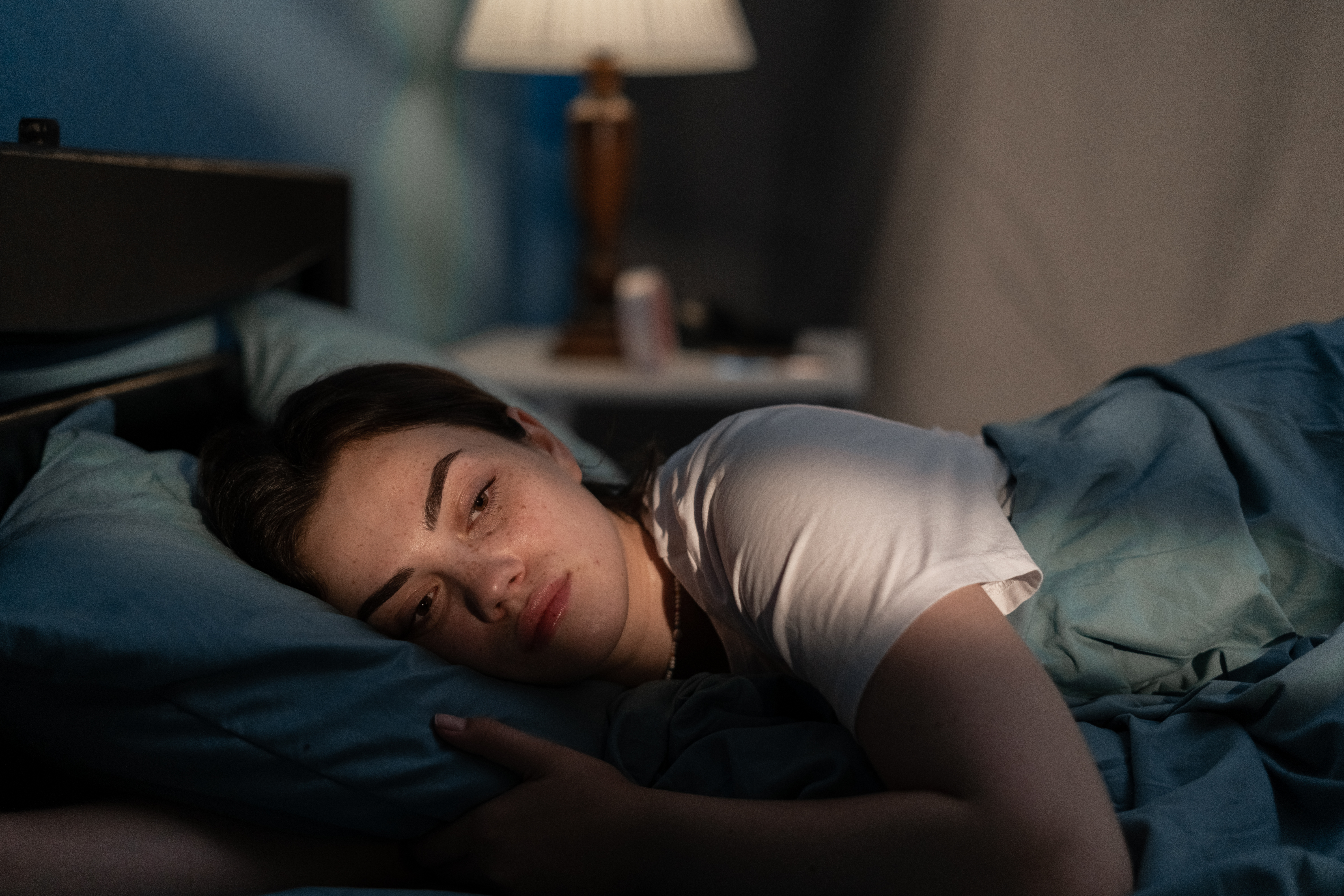 Young sad woman lying in bed late at night trying to sleep suffering insomnia. Girl in bed scared on nightmares looking worried and stressed. Sleeping disorder and insomnia | Source: Getty Images