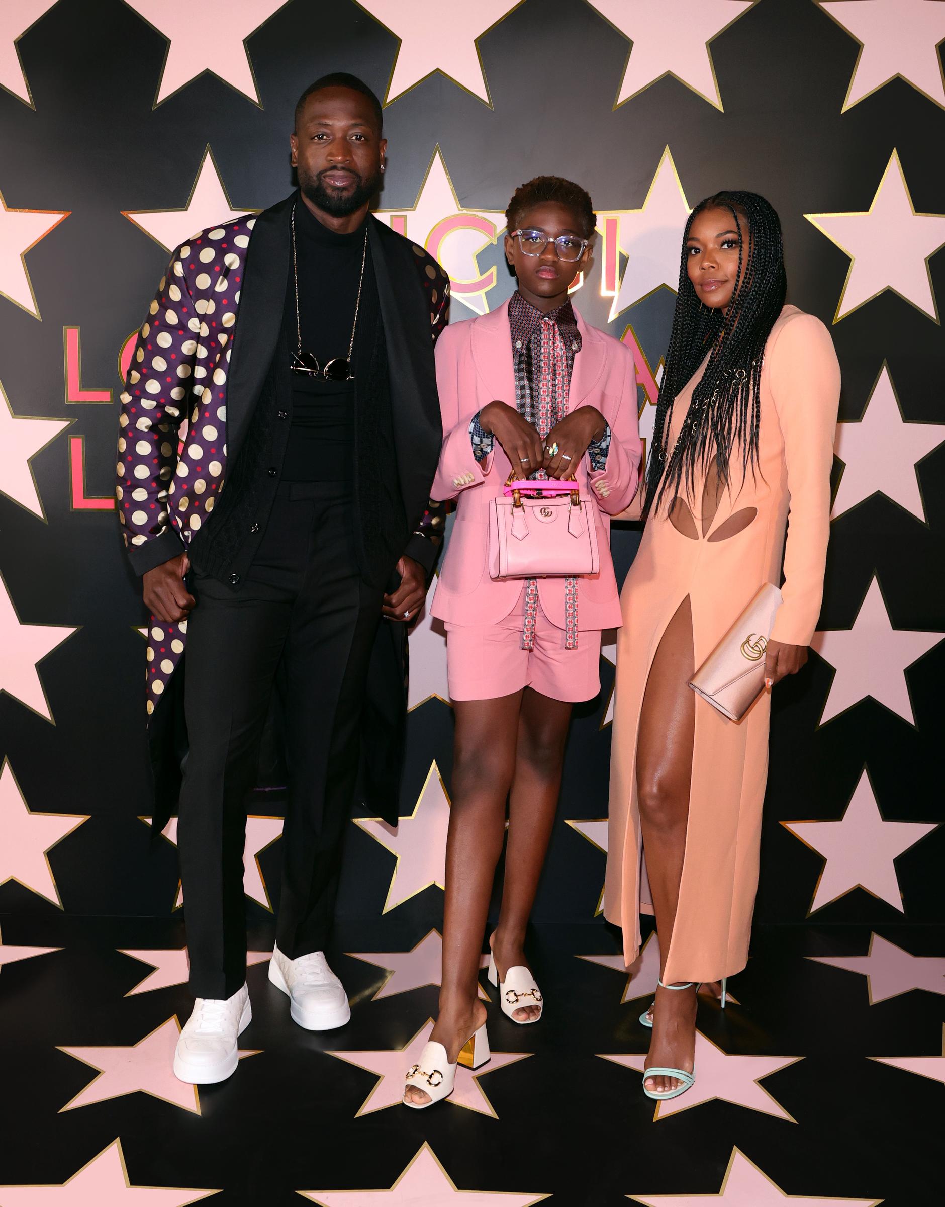 Dwyane Wade, Zaya Wade, and Gabrielle Union pose together before a star-patterned backdrop at the Gucci Love Parade, showcasing coordinated designer looks during the fashion event.