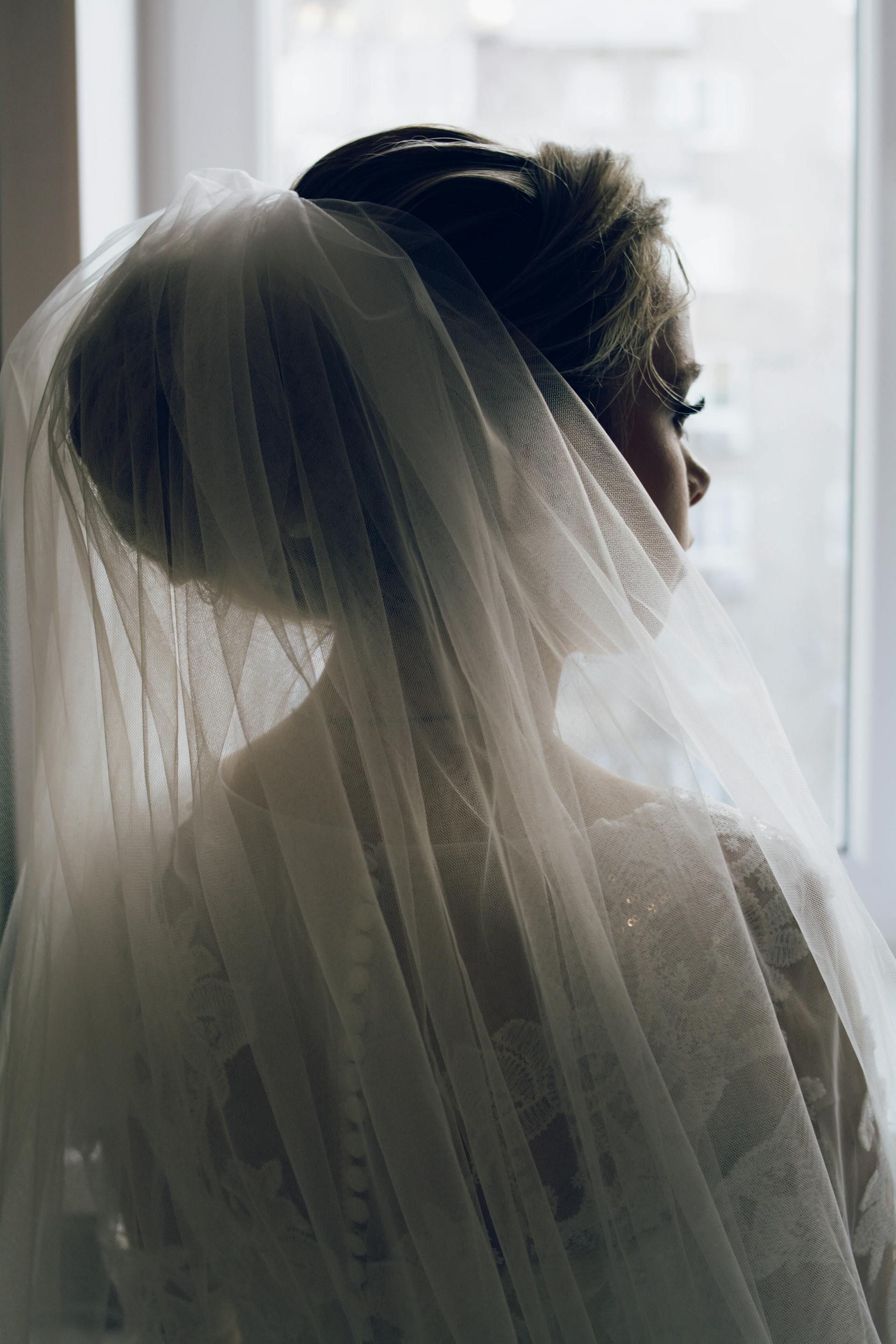 A bride in a wedding dress and veil looking through the window | Source: Pexels