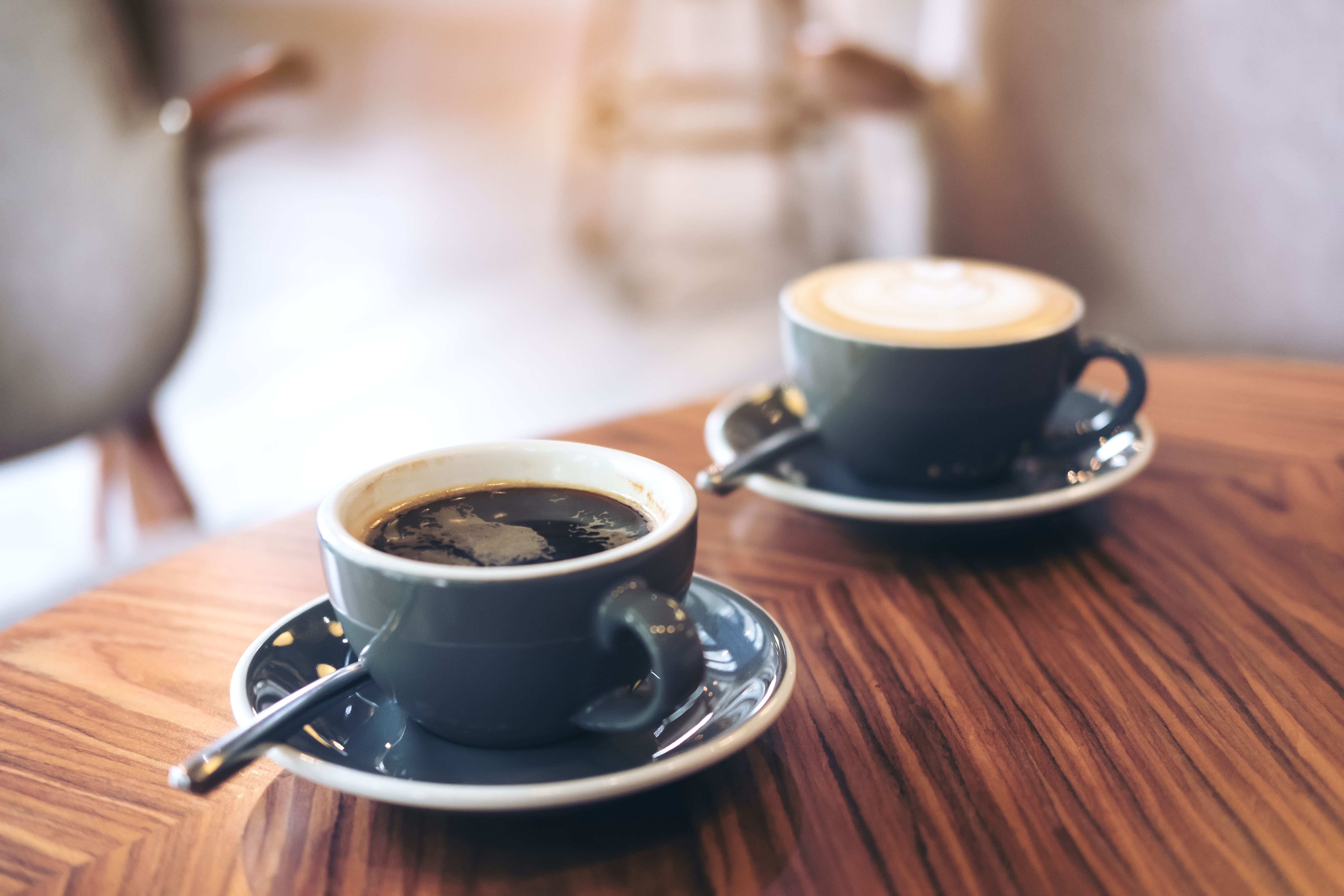 Closeup image of two blue cups of hot latte coffee and Americano coffee on vintage wooden table in cafe | Source: Shutterstock