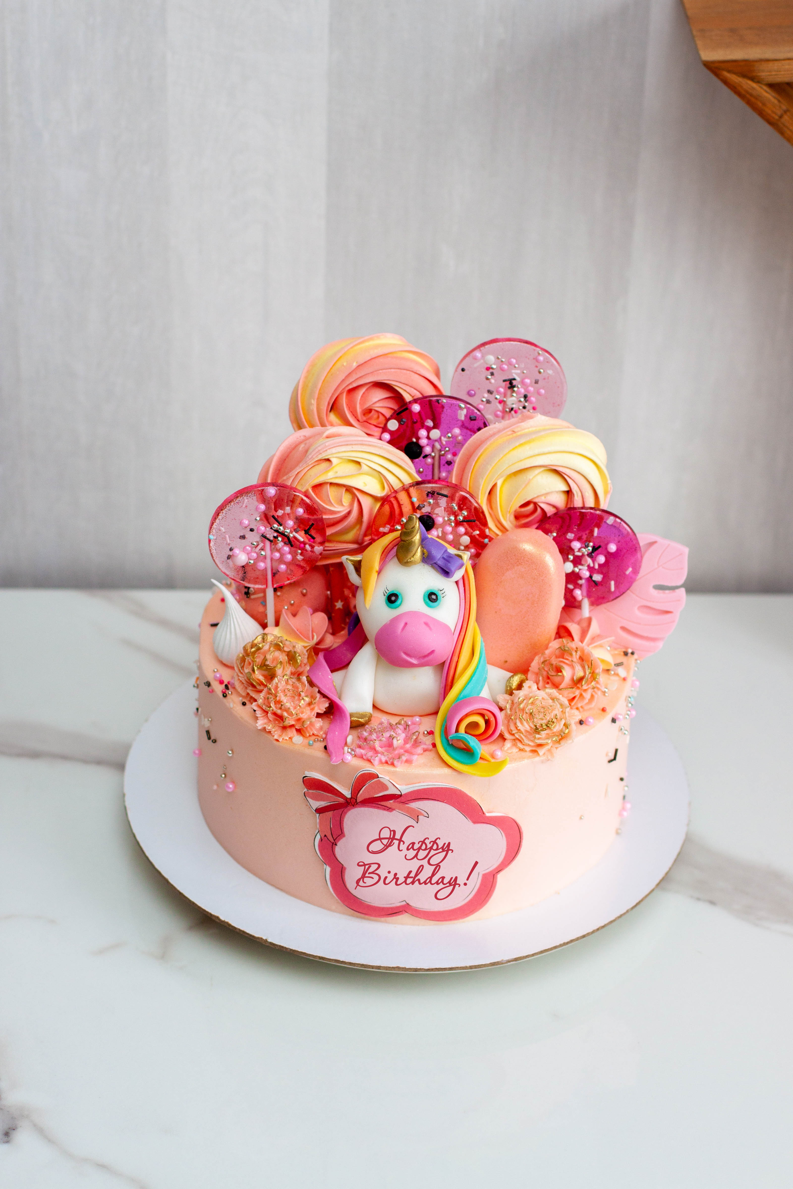 Birthday cake with cute fondant unicorn, lollipos, meringues, popsicles and chocolate flowers for a girl or a baby. Text Happy Birthday | Source: Getty Images