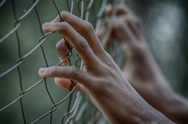 Hands holding on to the fence. | Source: PixaBay