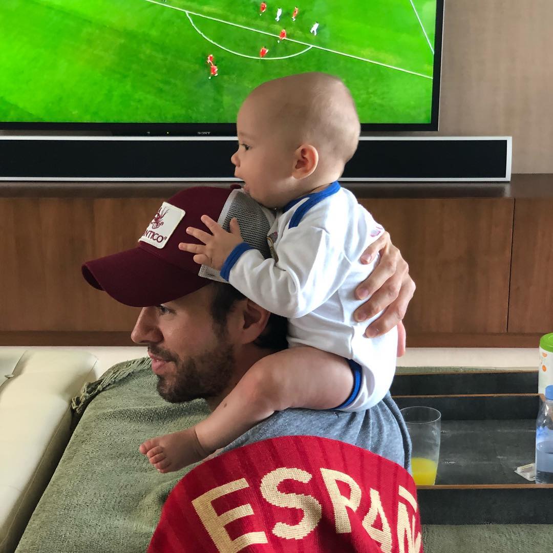 Enrique Iglesias holding Nicholas Iglesias on his shoulders while a soccer game plays in the background, from a post dated June 15, 2018 | Source: Instagram/enriqueiglesias