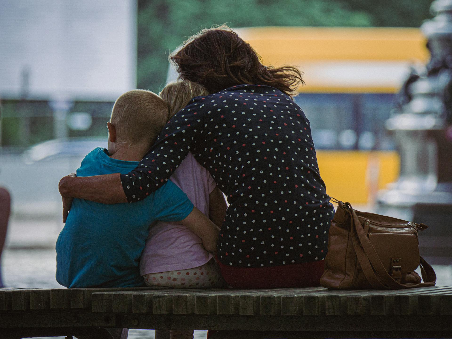 A back view shot of a woman hugging her kids while sitting on a bench | Source: Pexels