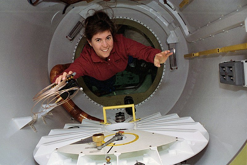 Mission Specialist Janice Voss, holding a camera, cable, & batteries, floats through the spacelab tunnel adapter on her way to the SPACEHAB module aboard Endeavour | Source: Wikimedia Commons