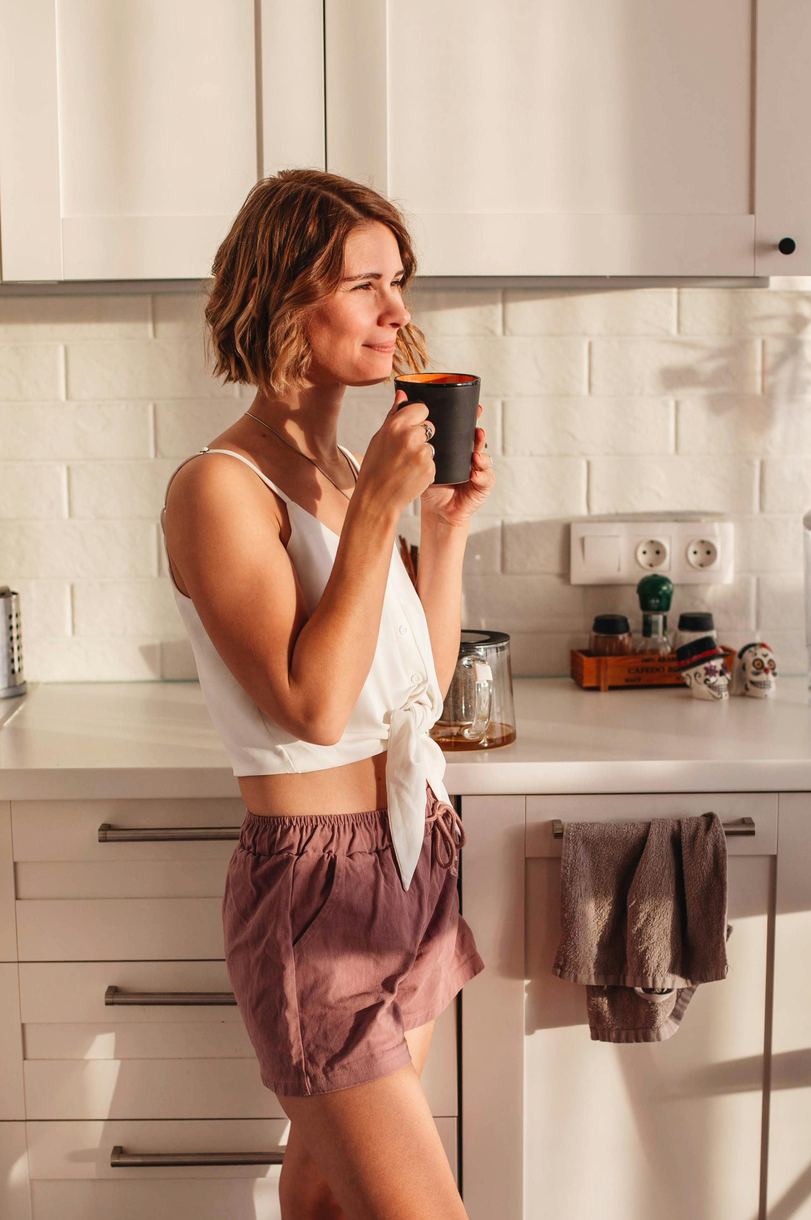 A happy woman holding a cup of coffee in the kitchen | Source: Pexels