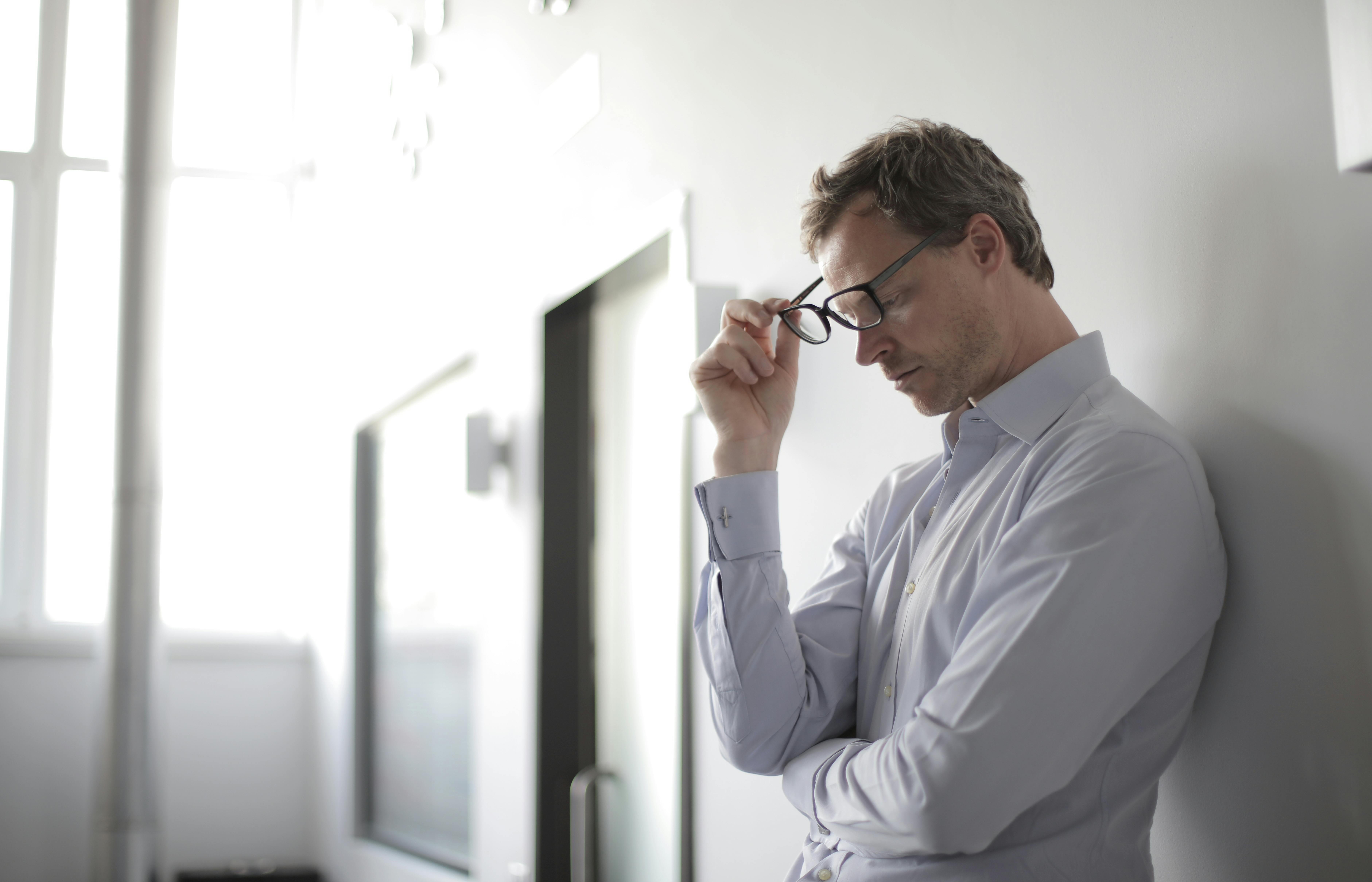An upset man leaning against a wall and removing his glasses | Source: Pexels