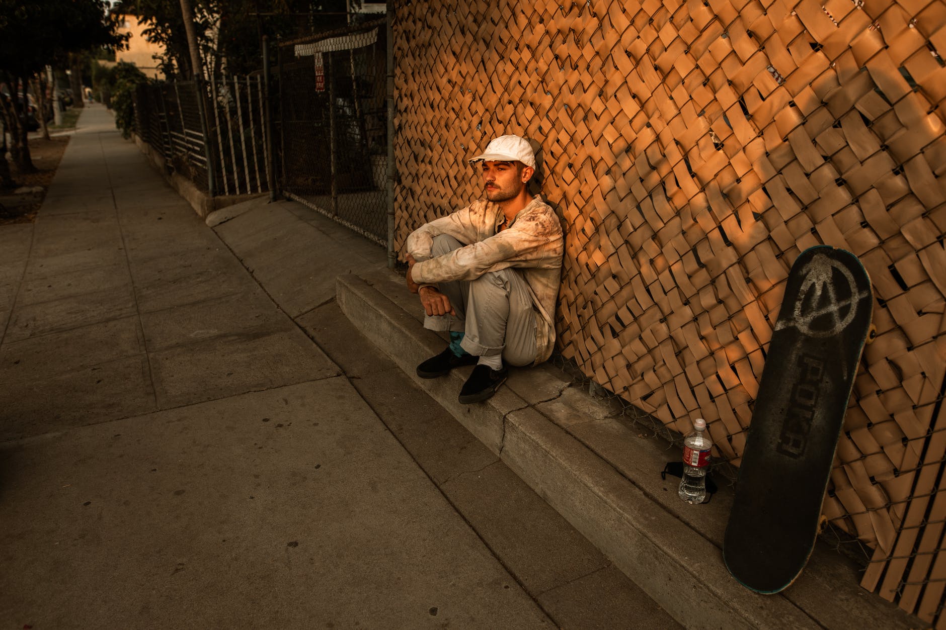 Un hombre sentado recostado de una pared cerca de una patineta. | Foto: Pexels