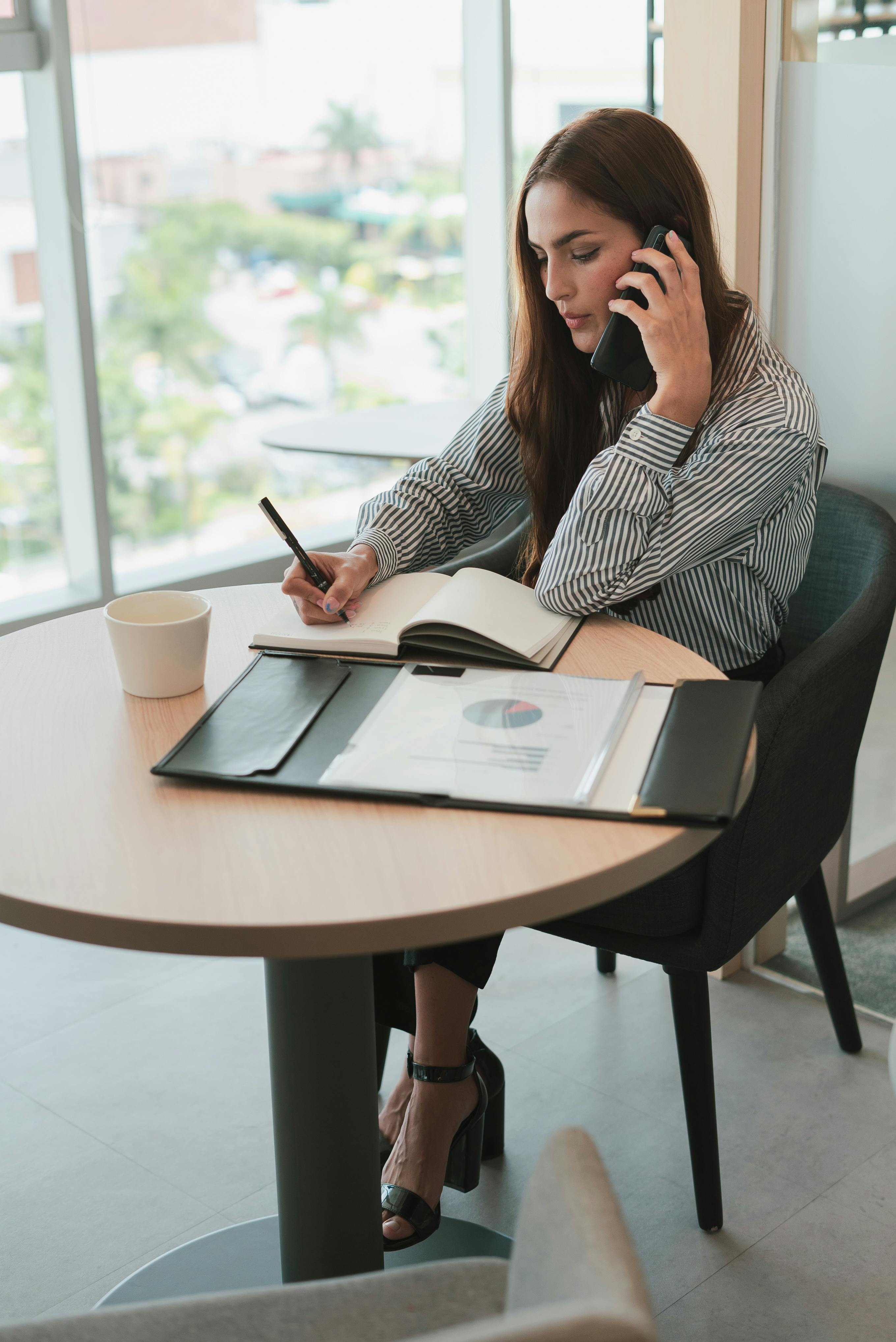 A woman writing something down while on a phone call | Source: Pexels