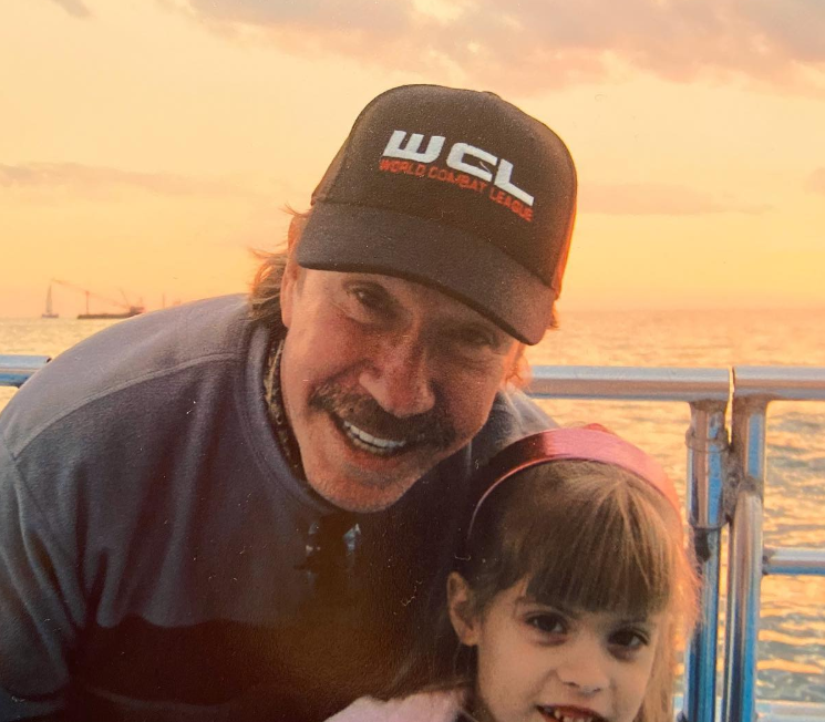 Against a glowing sunset by the water, Chuck Norris leans in close beside little Danilee Norris, their faces lit with warmth as they share a quiet, happy snapshot together. | Source: Instagram/d.ani.lee