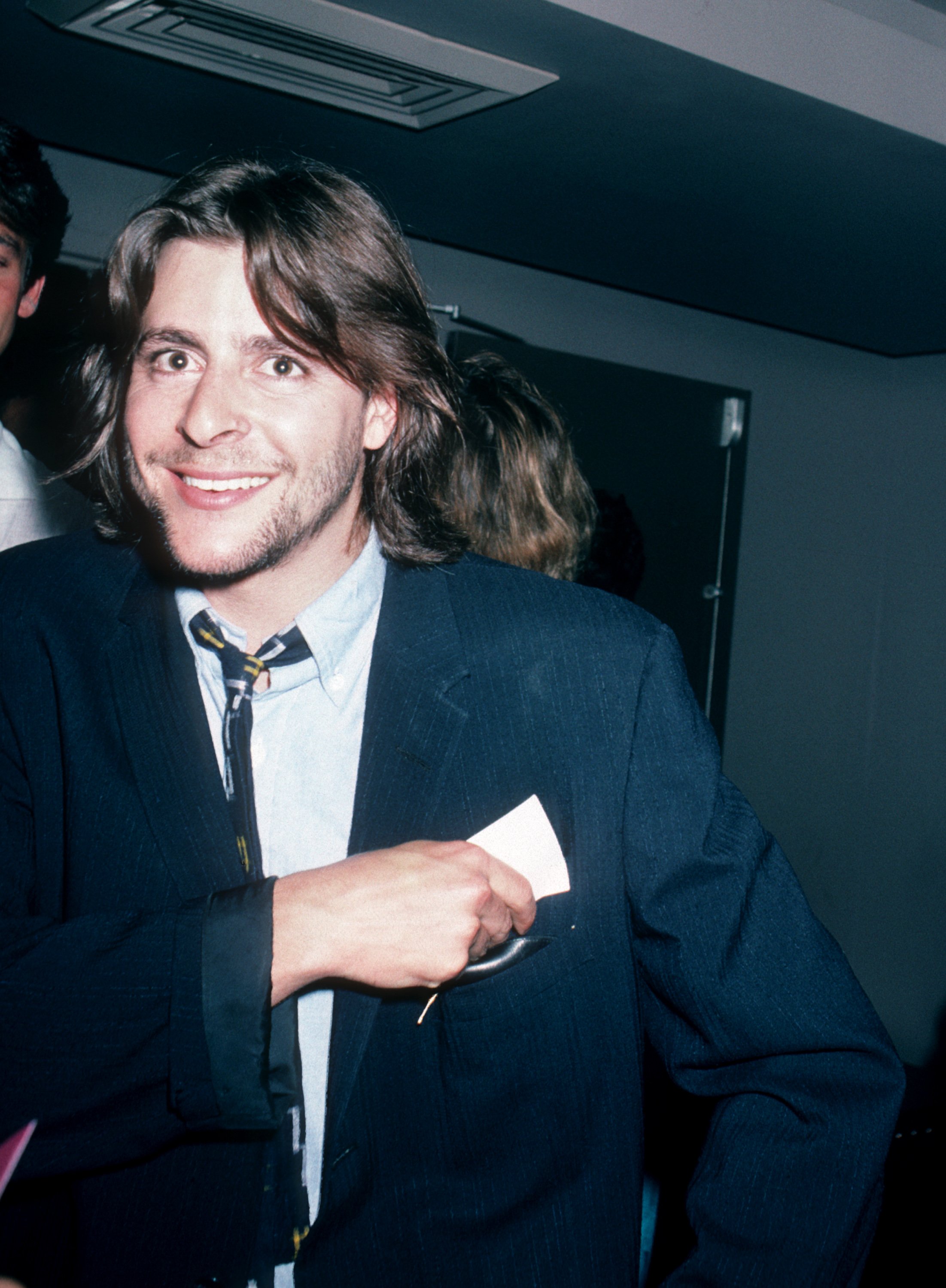 Flashing a warm smile while slipping a card into his jacket pocket, the young actor enjoyed an evening out at the Peter Max Art Exhibit at Marylou's in New York City in 1986. | Source: Getty Images