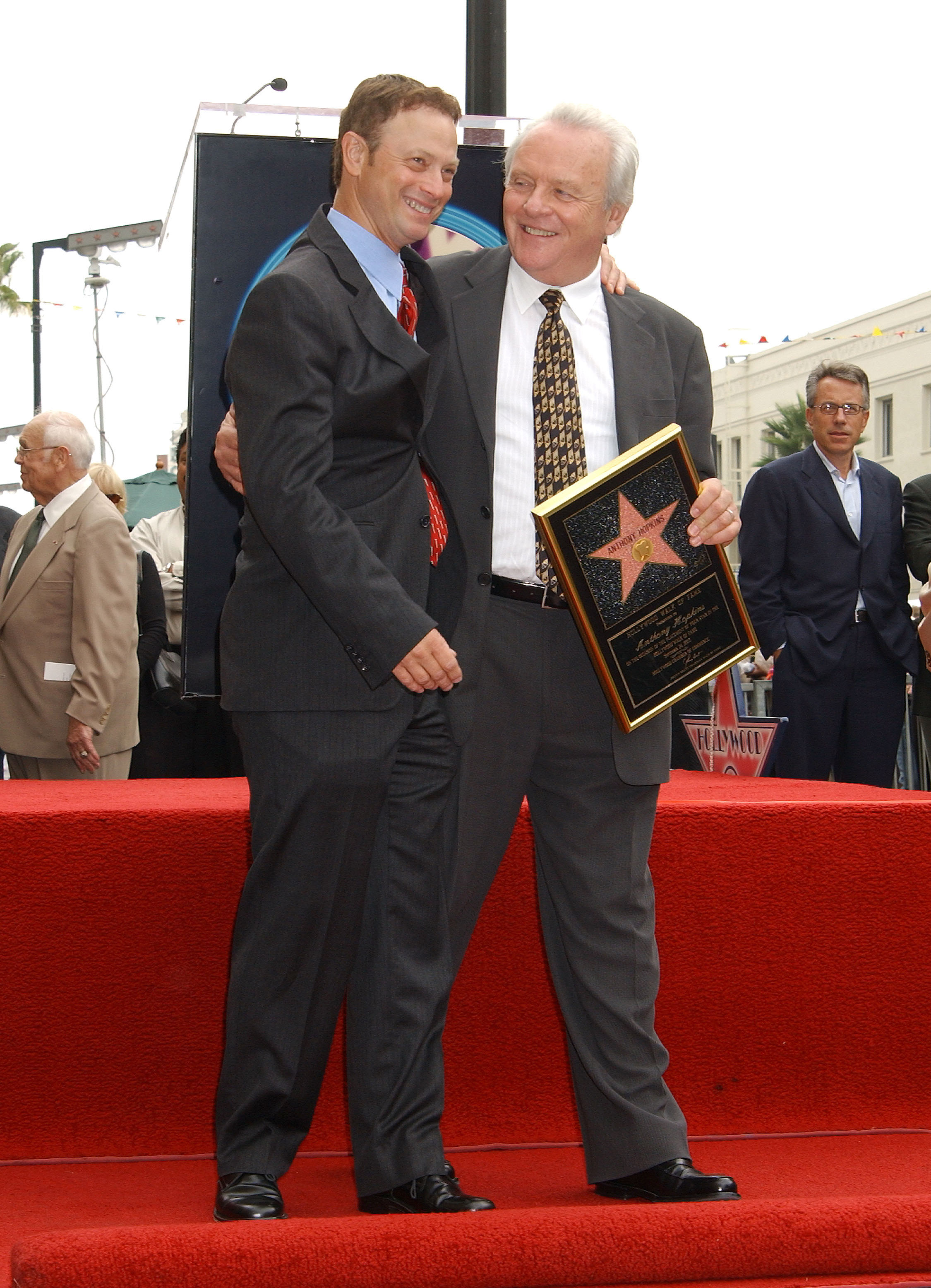 Anthony Hopkins embraces Gary Sinise warmly as they celebrate on the iconic red carpet of the Hollywood Walk of Fame. Holding his commemorative plaque, Hopkins beams with gratitude and pride. The moment captures camaraderie, respect, and the joy of a well-earned honor in Hollywood's storied tradition.