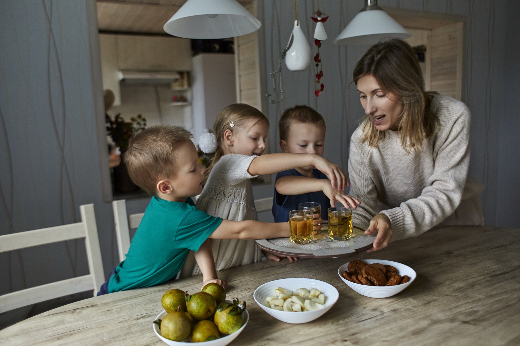 Una madre con sus tres hijos compartiendo una merienda en la cocina. | Foto: Getty Images