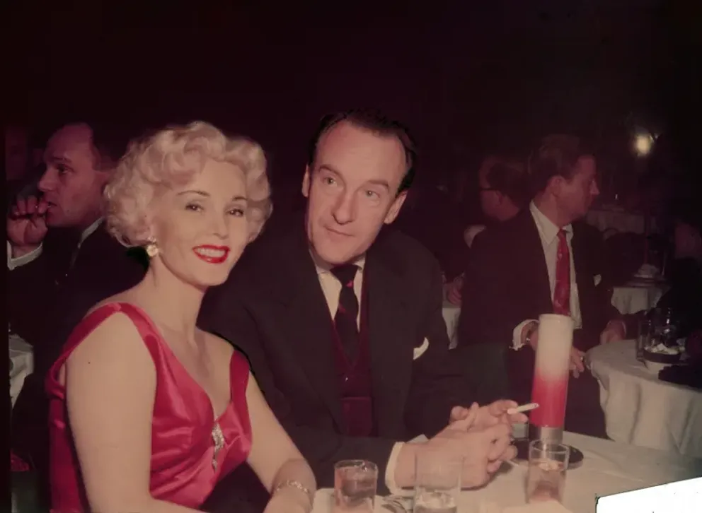 Zsa Zsa Gabor sourit, assise à une table avec son mari, l'acteur britannique George Sanders, dans les années 1950 | Photo : Getty Images