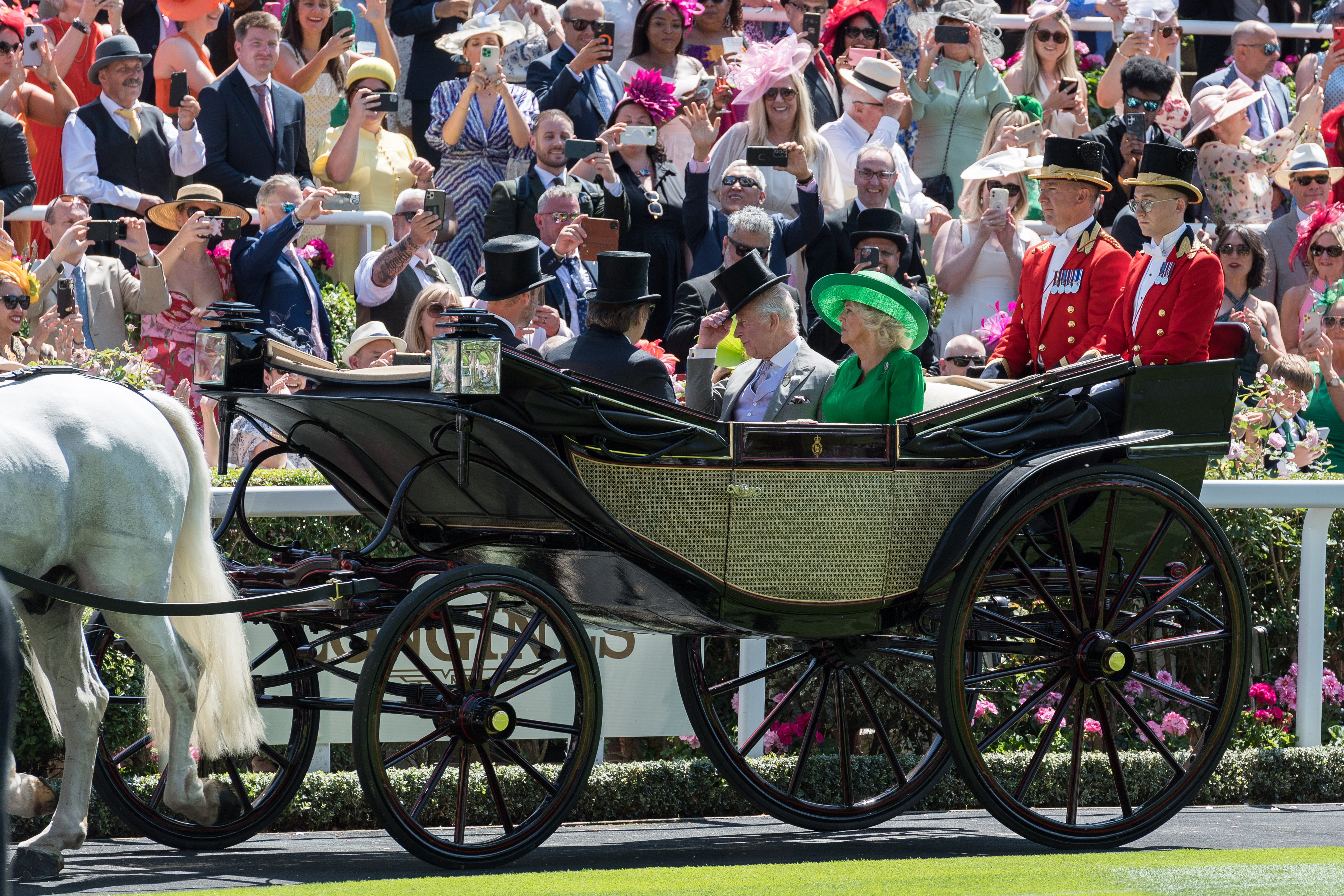 King Charles III, Queen Camilla, Prince Saud bin Khalid Al-Saud, and Prince William make a regal entrance in a horse-drawn carriage on the second day of Royal Ascot, drawing cheers from the crowd.