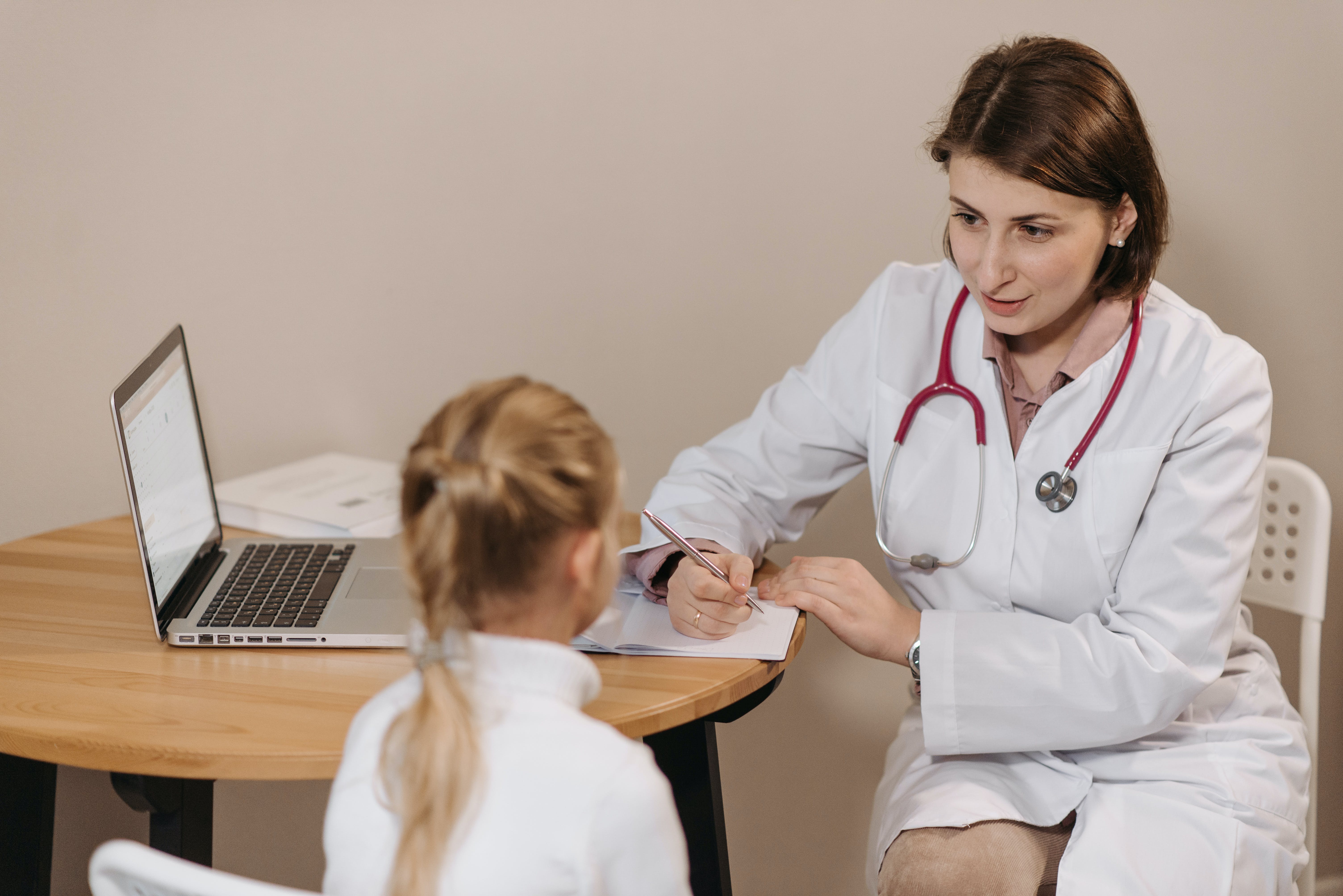 A doctor listening to a little girl while taking notes. | Source: Pexels