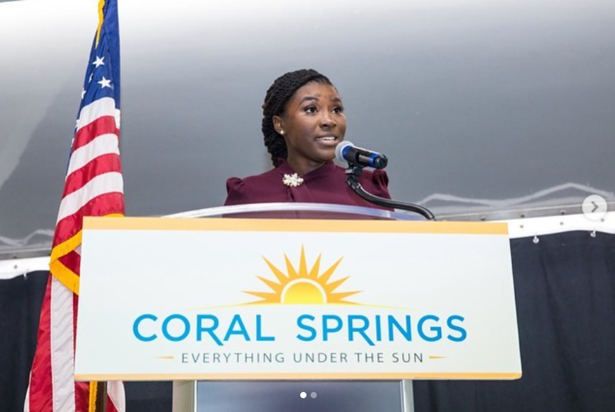 Standing at the podium in Coral Springs, Nancy Metayer Bowen speaks with clarity and conviction, framed by the city’s emblem — her posture and expression reflecting confident, public-facing leadership. | Source: Instagram/nancymetayerbowen