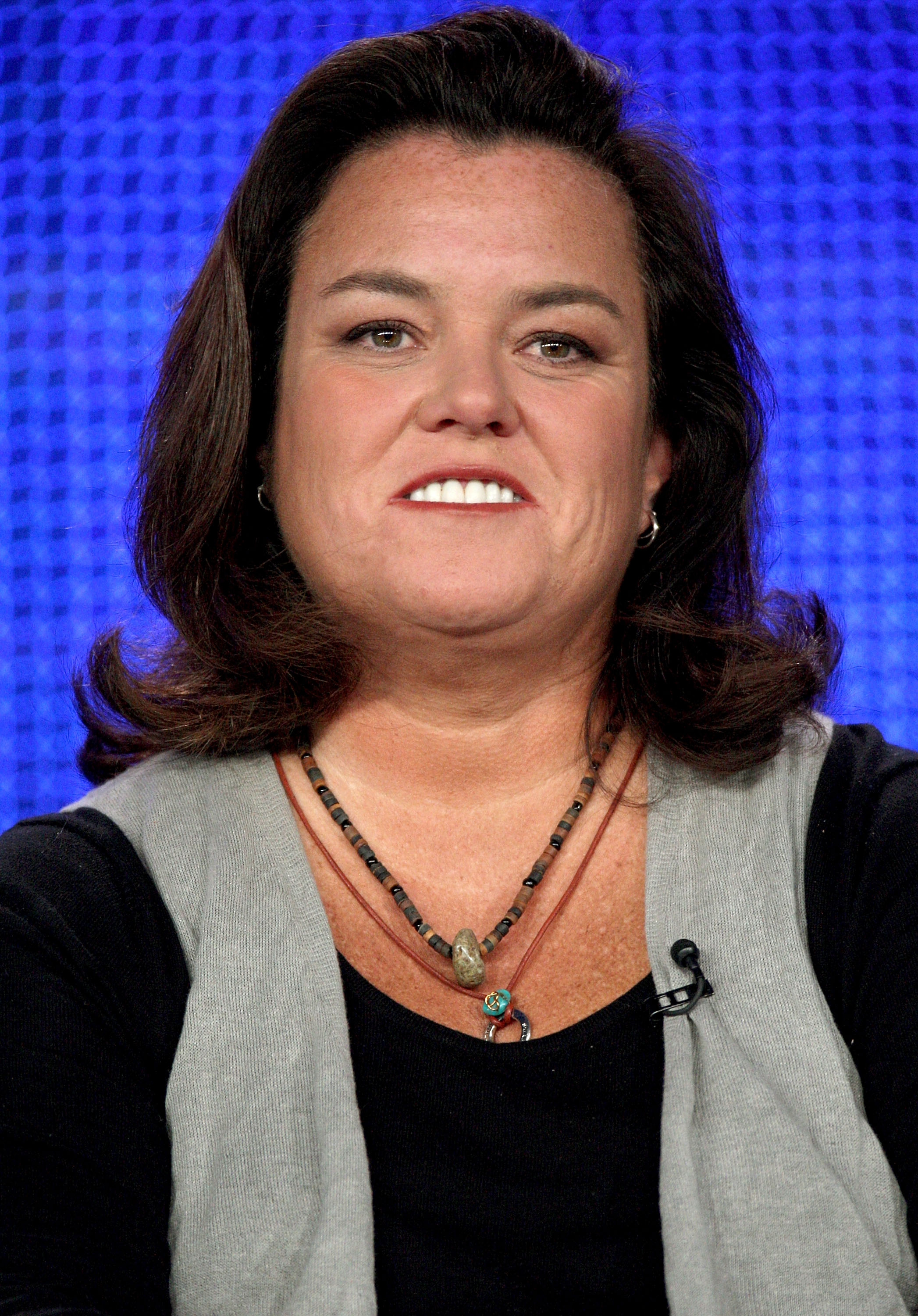 Rosie O'Donnell speaks during the HBO portion of the Television Critics Association press tour in Pasadena, smiling onstage against a vivid blue screen backdrop.