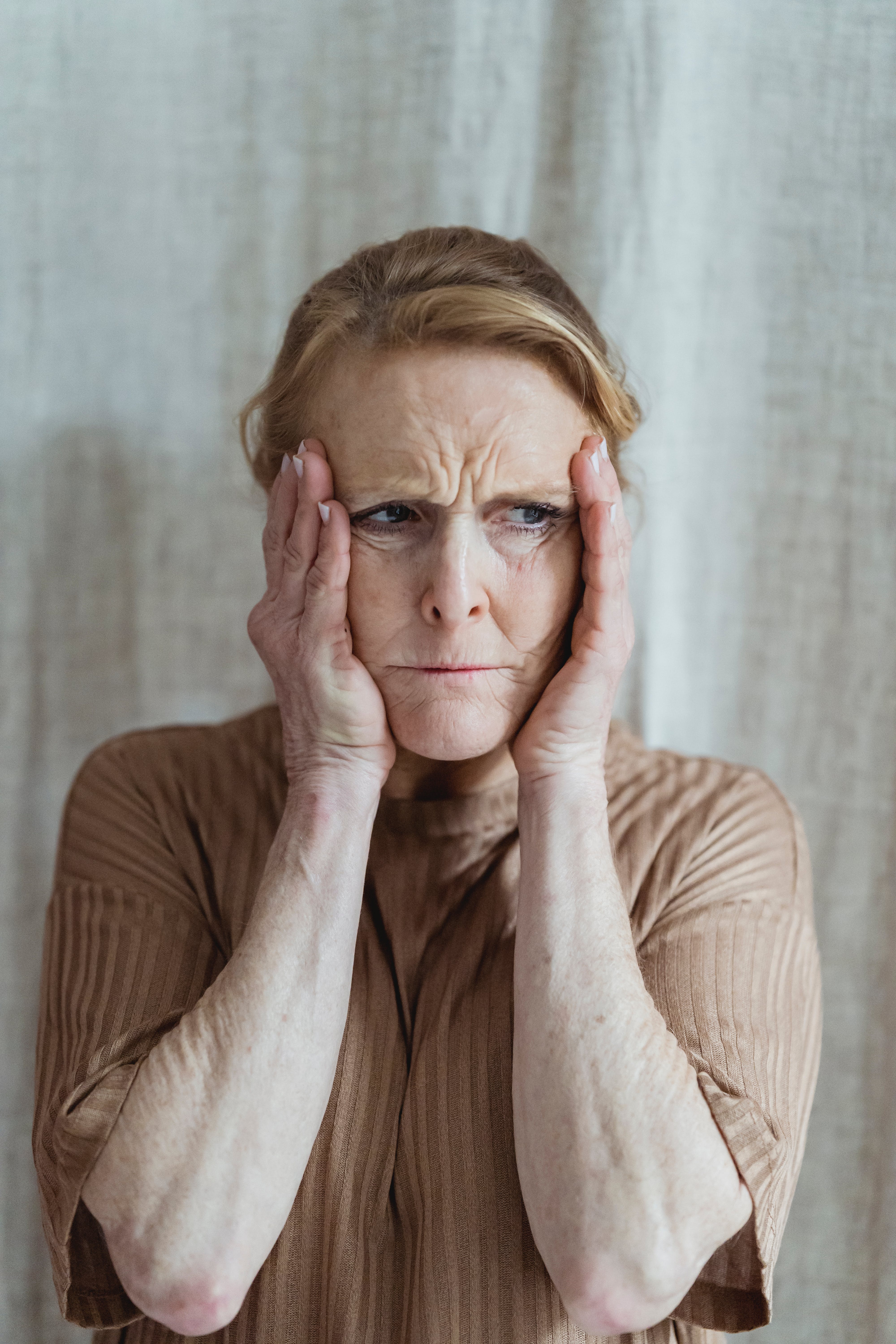 A distressed older woman holding her face with both hands | Source: Pexels
