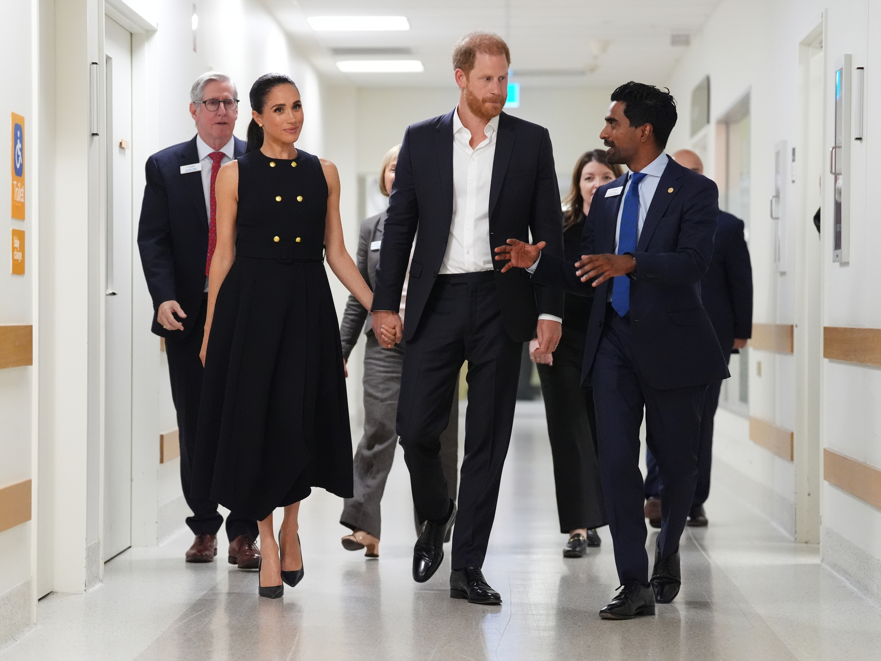 The Duke and Duchess of Sussex walk hand in hand through a hospital corridor, speaking with staff during their Melbourne visit on 14 April 2026. | Source: Getty Images