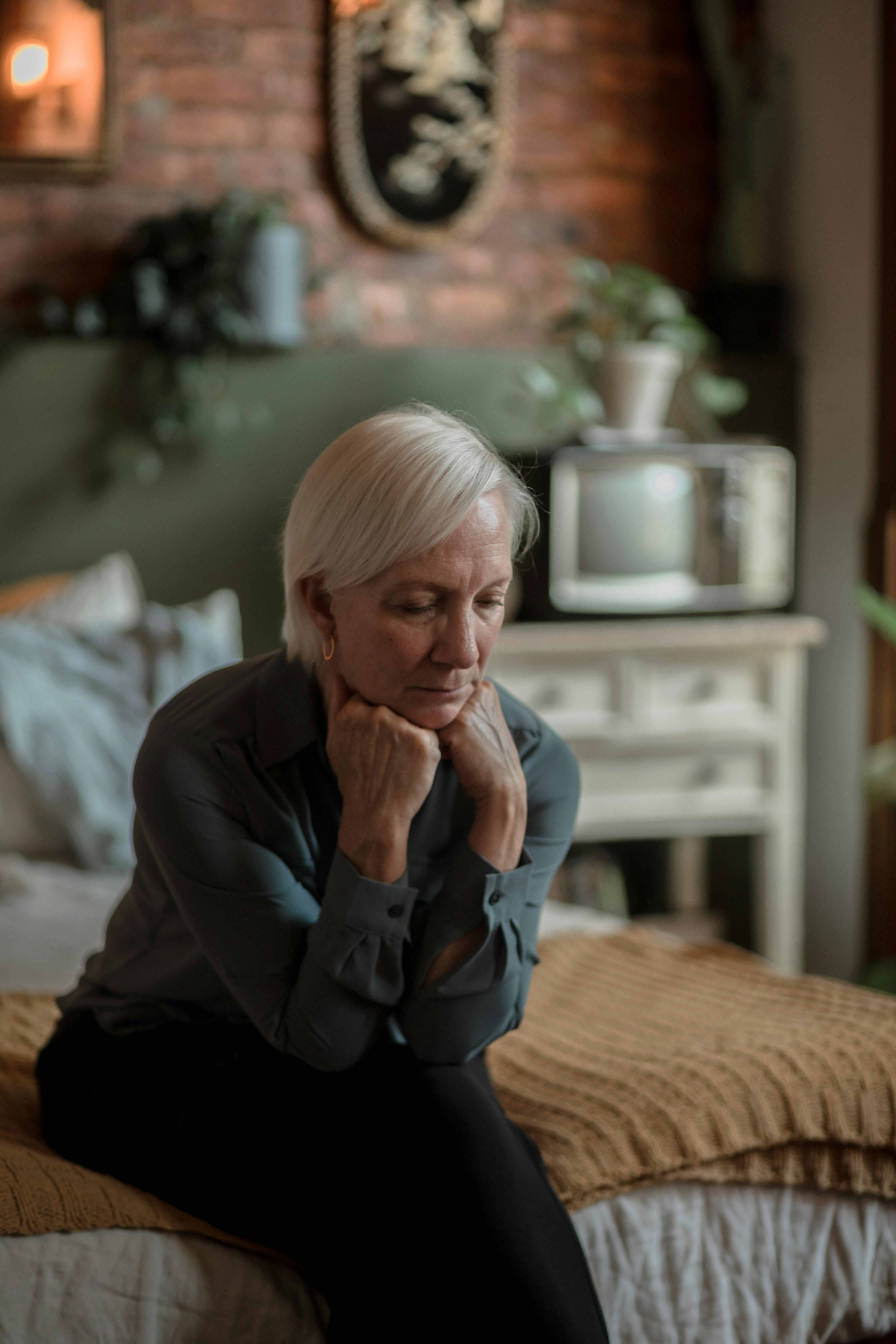 An upset elderly woman sitting on her bed | Source: Pexels