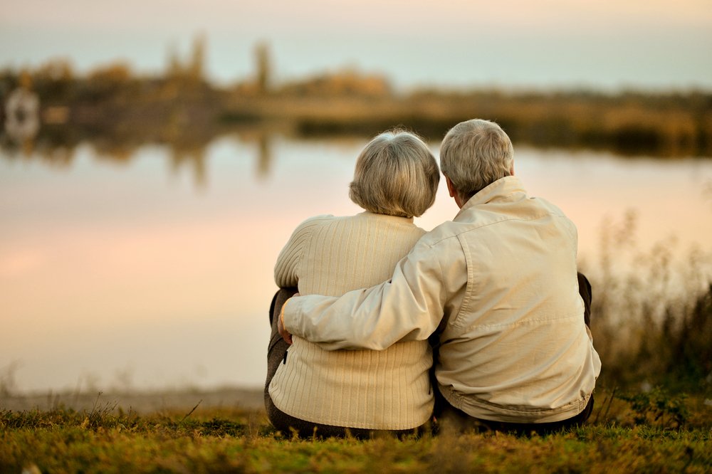 Par de abuelitos abrazados sentados a la orilla de un lago. | Foto: Shutterstock