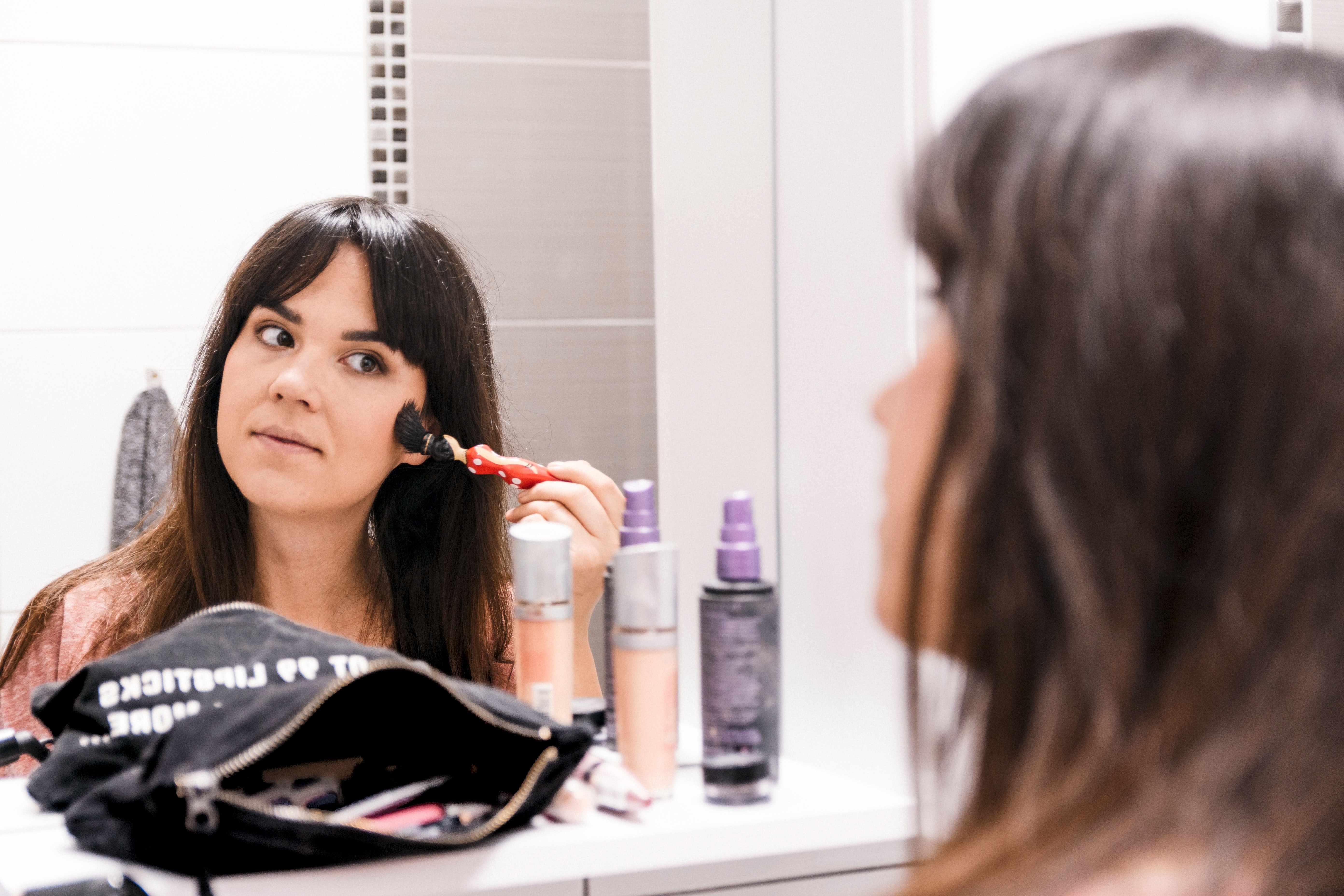 Une femme se maquiller devant un miroir. | Photo : Pexels