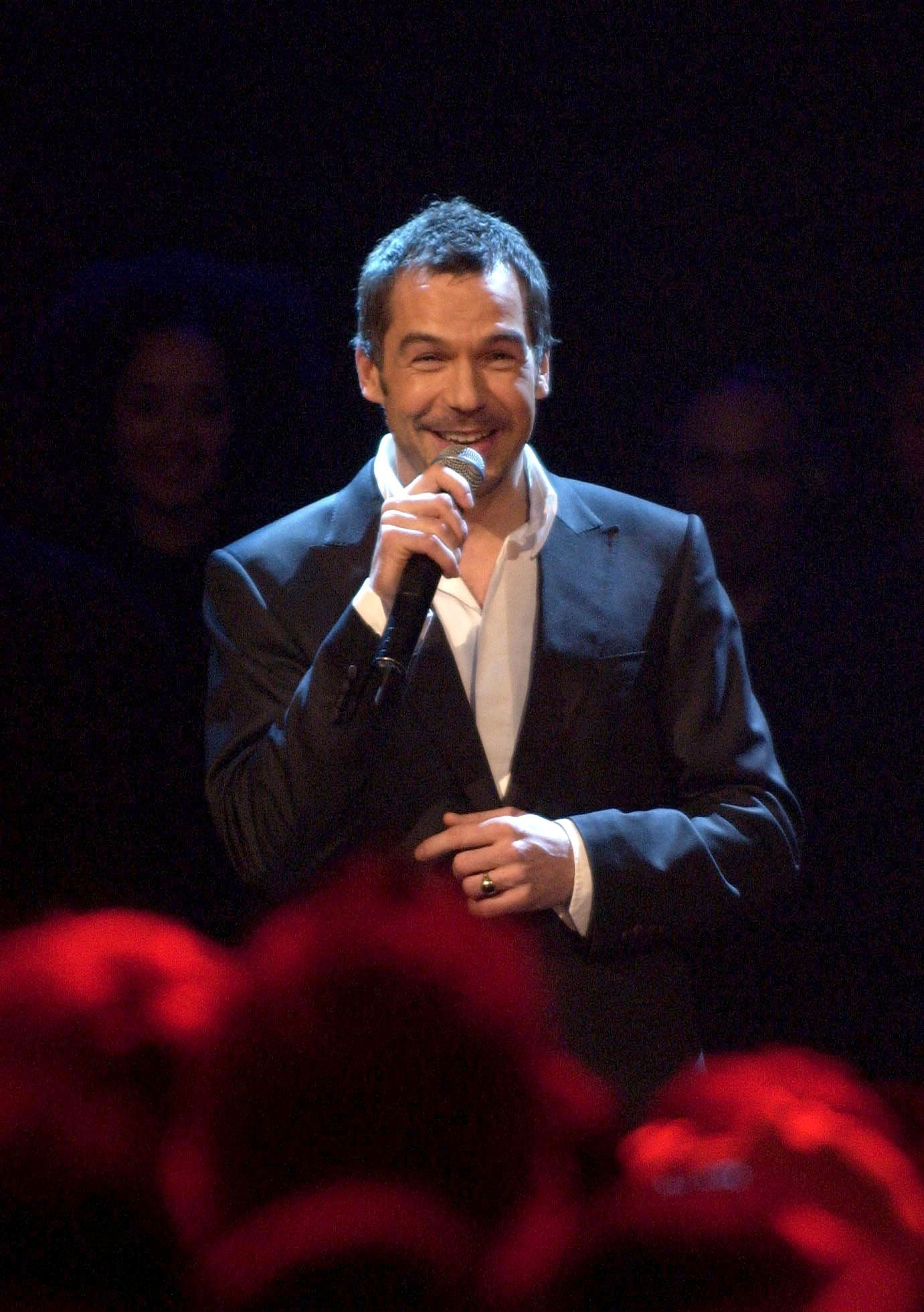 A fresh-faced Brookstein, clad in a navy suit and open-collar white shirt, beams mid-performance at the Radio One and Top of the Pops Christmas Party at the Shepherds Bush Empire, London, in December 2004 — just days after being crowned "X Factor" champion.