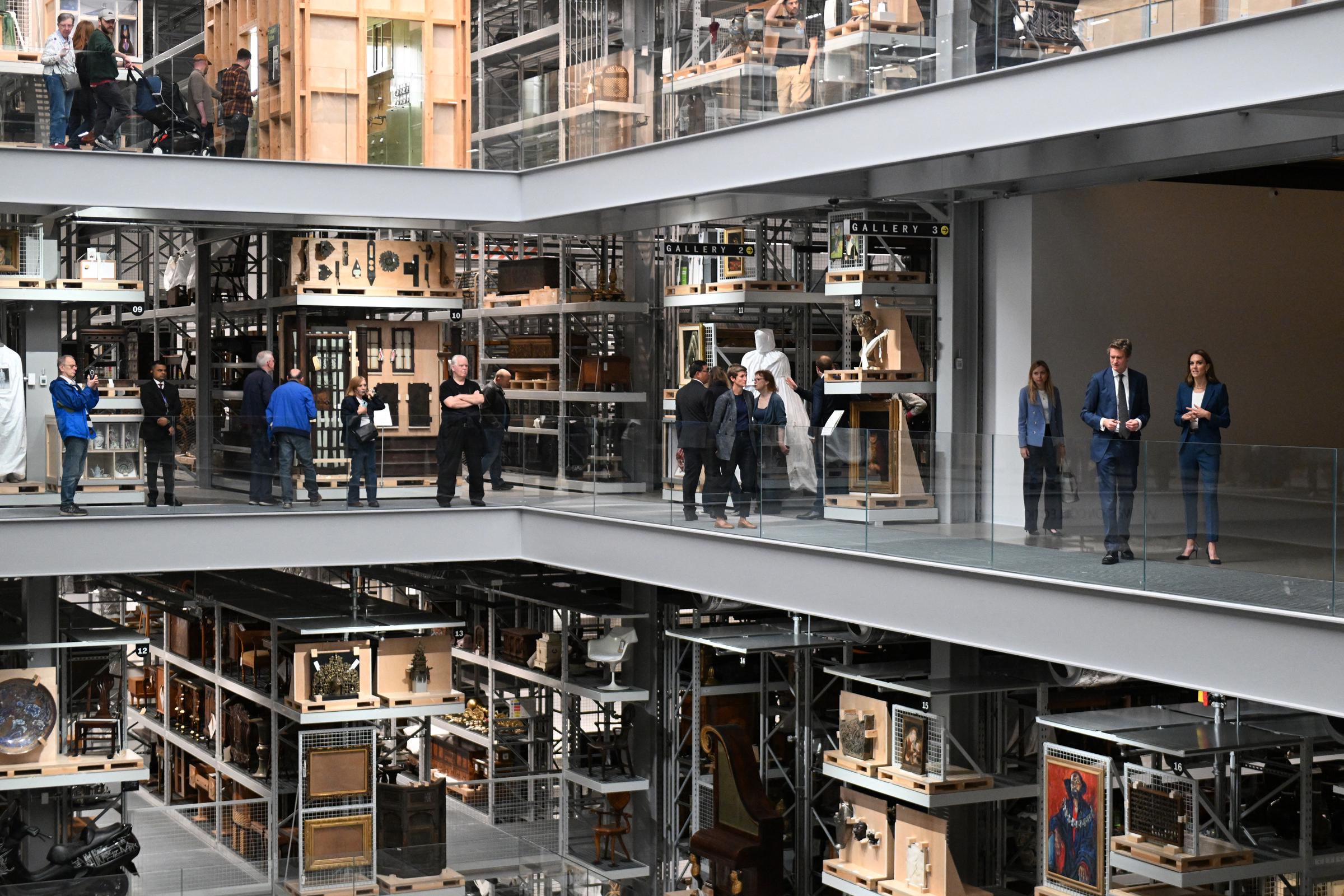 Seen from a distance, Princess Catherine walks beside Tristram Hunt through the gallery mezzanine. With shelves of art and artifacts lining the path, she listens closely, her expression composed and observant.