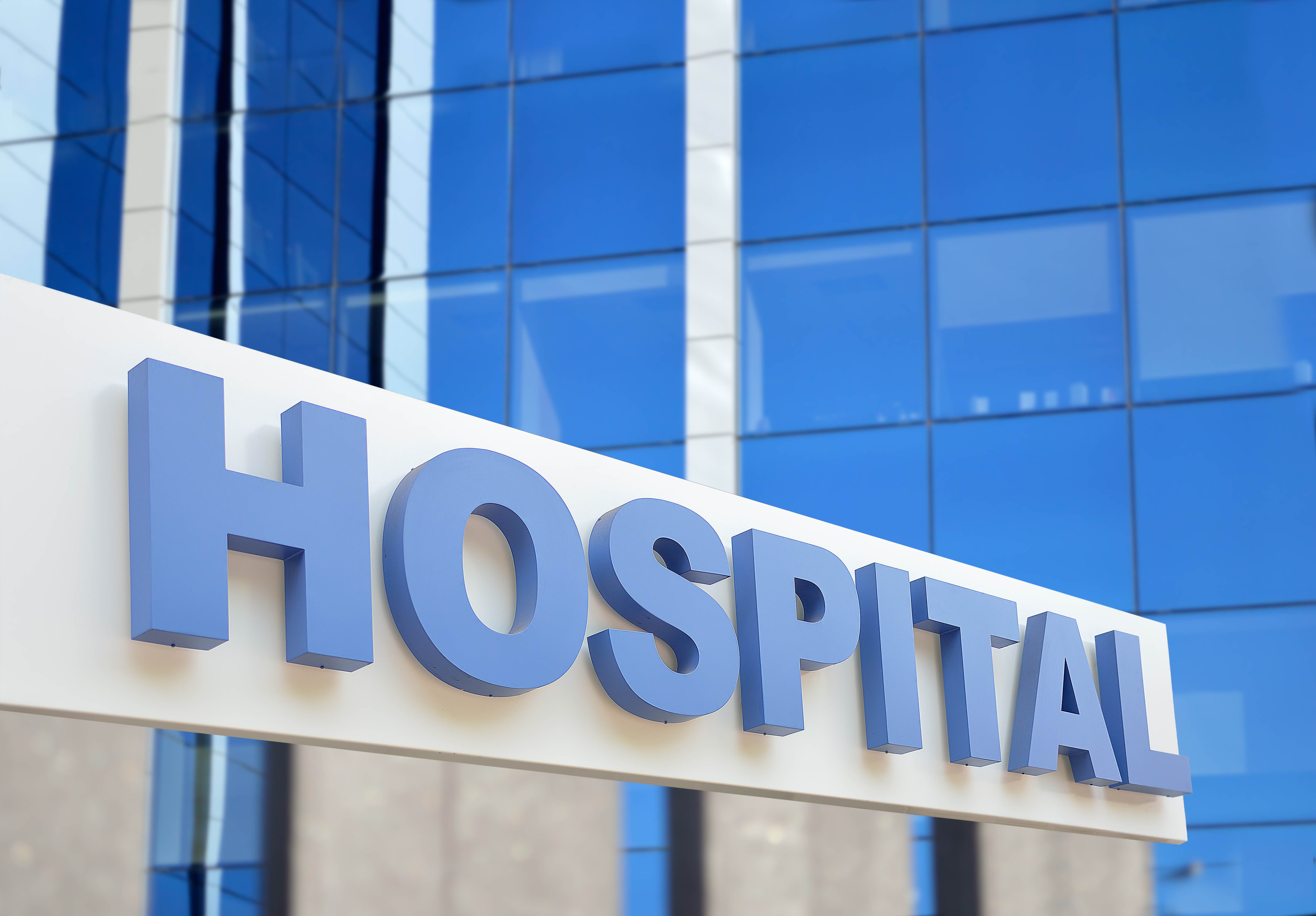 Hospital building sign closeup, with sky reflecting in the glass. | Source: Shutterstock