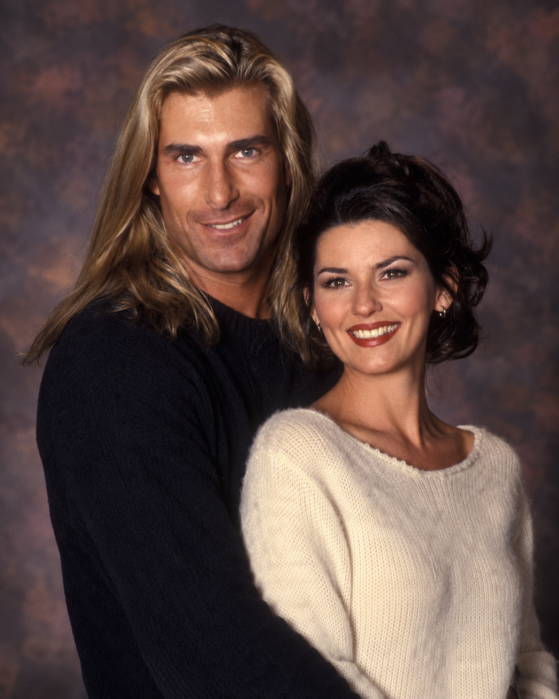 In an AI-generated portrait, Fabio embraces Shania Twain from behind as they pose in cozy knit sweaters, capturing a warm mid-1990s studio look. | Source: ChatGPT