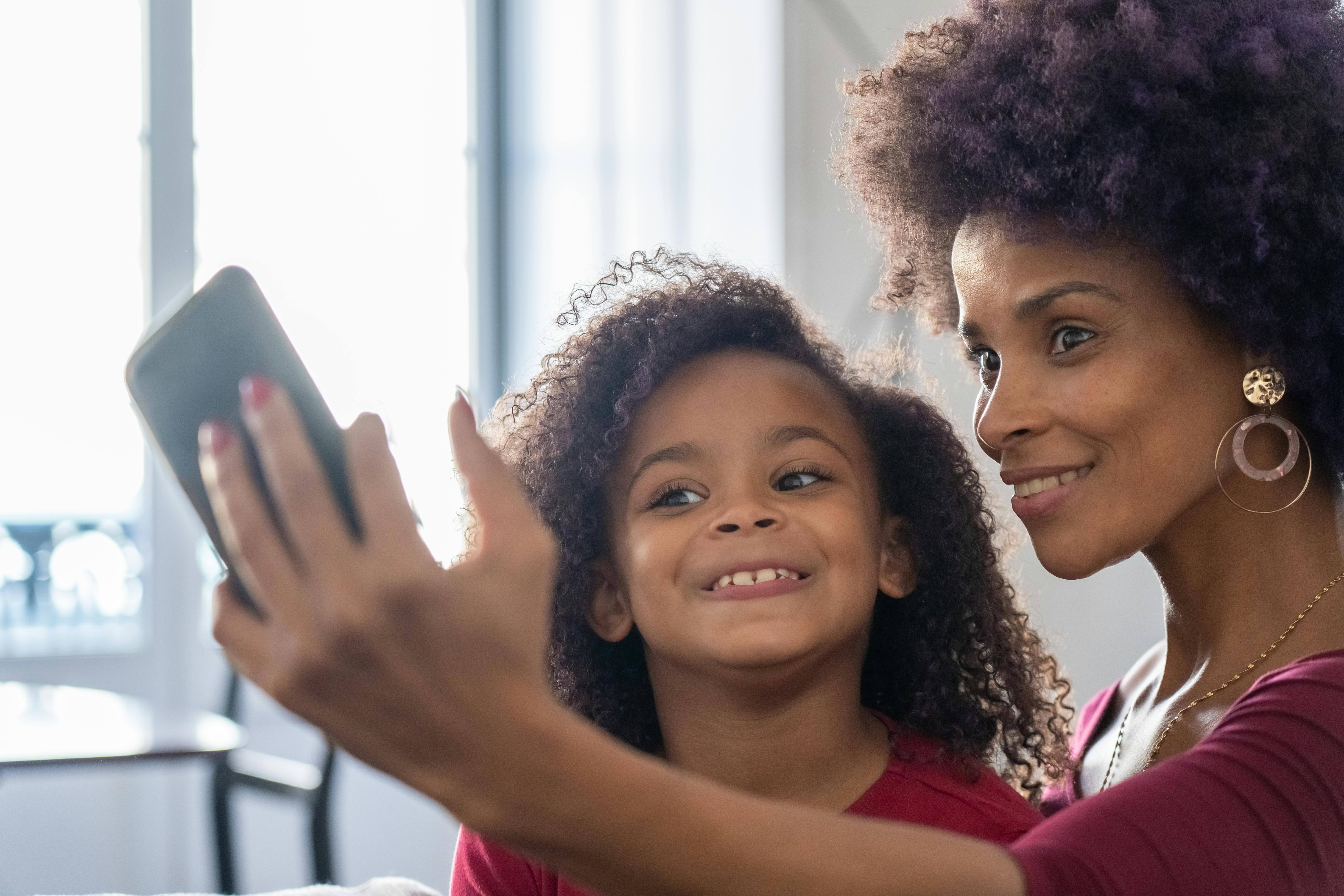 A woman smiling while posing for a selfie with gold earrings as her daughter looks on | Source: Pexels