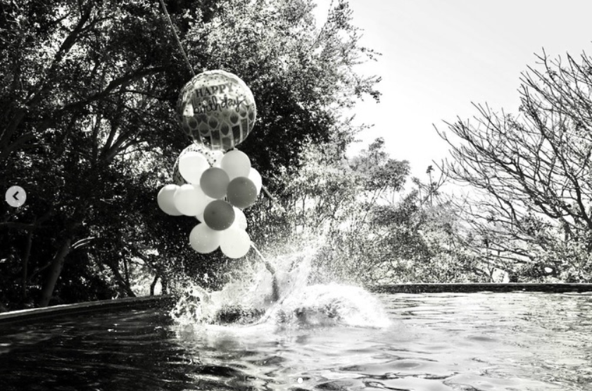 Meghan shared a playful moment from her 45th birthday, swinging into a pool while holding birthday balloons. She wore a dark one-piece swimsuit and oversized sunglasses for the relaxed celebration. | Source: Instagram/meghan