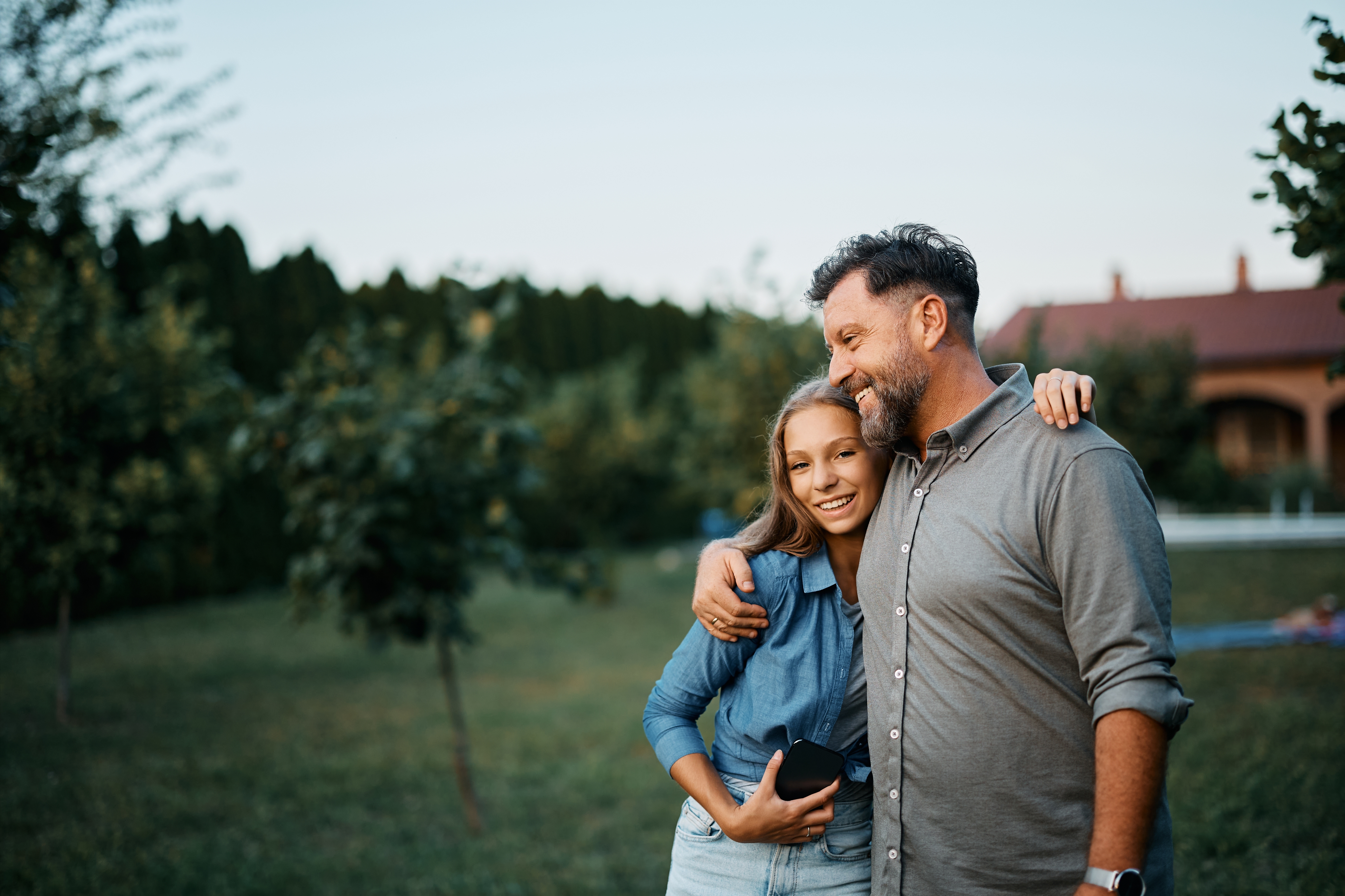 A happy father hugs his teenage daughter in the backyard | Source: Shutterstock