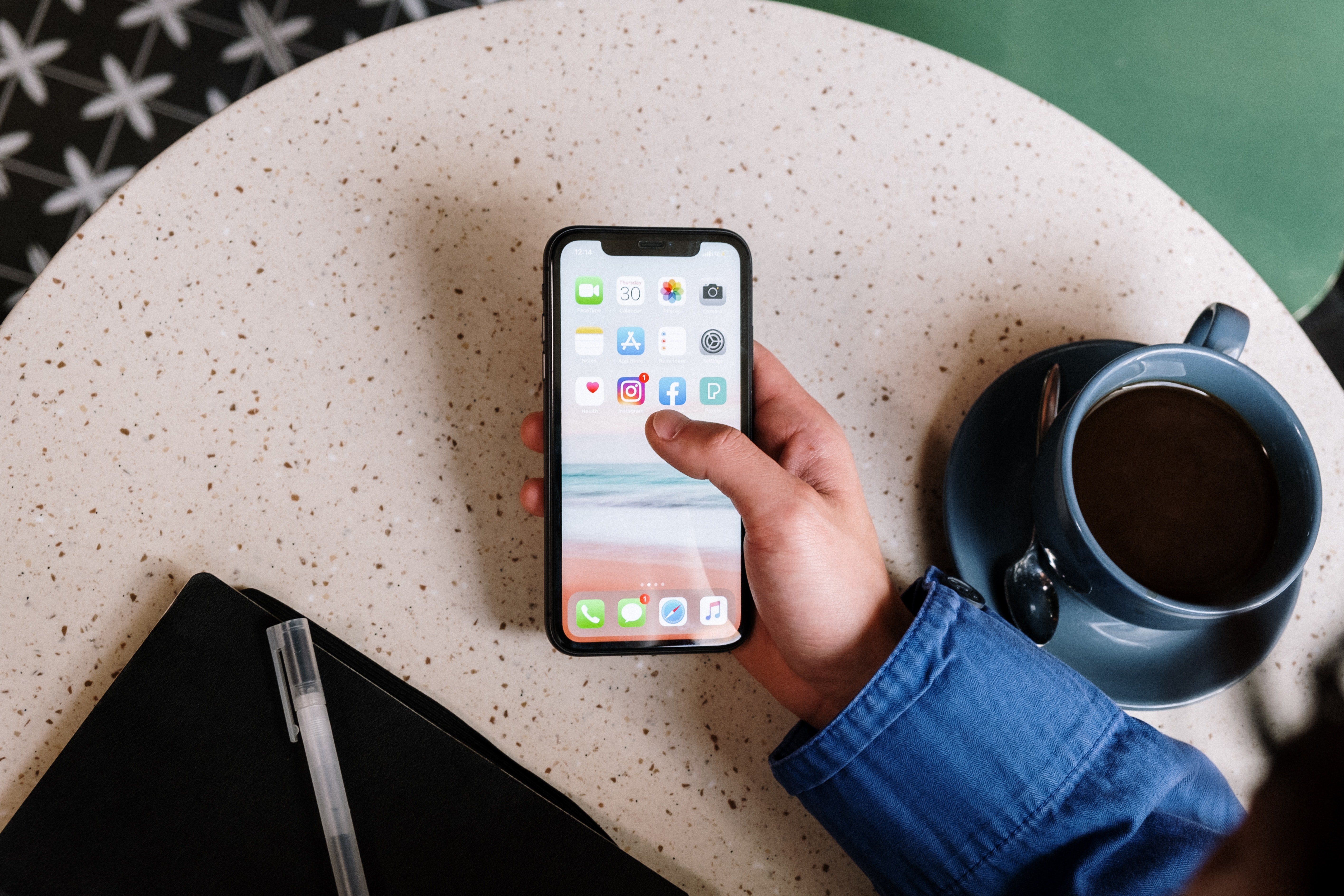 A hand holding a cellphone next to a cup of coffee | Photo: Pexels
