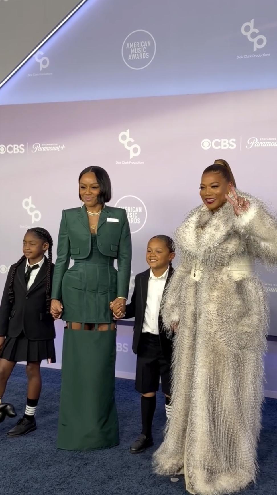 Eboni Nichols and Queen Latifah pose with Rebel Nichols Owens and Kaavia James Union Wade on the blue carpet beneath the glowing AMAs backdrop. | Source: Instagram/perezhilton