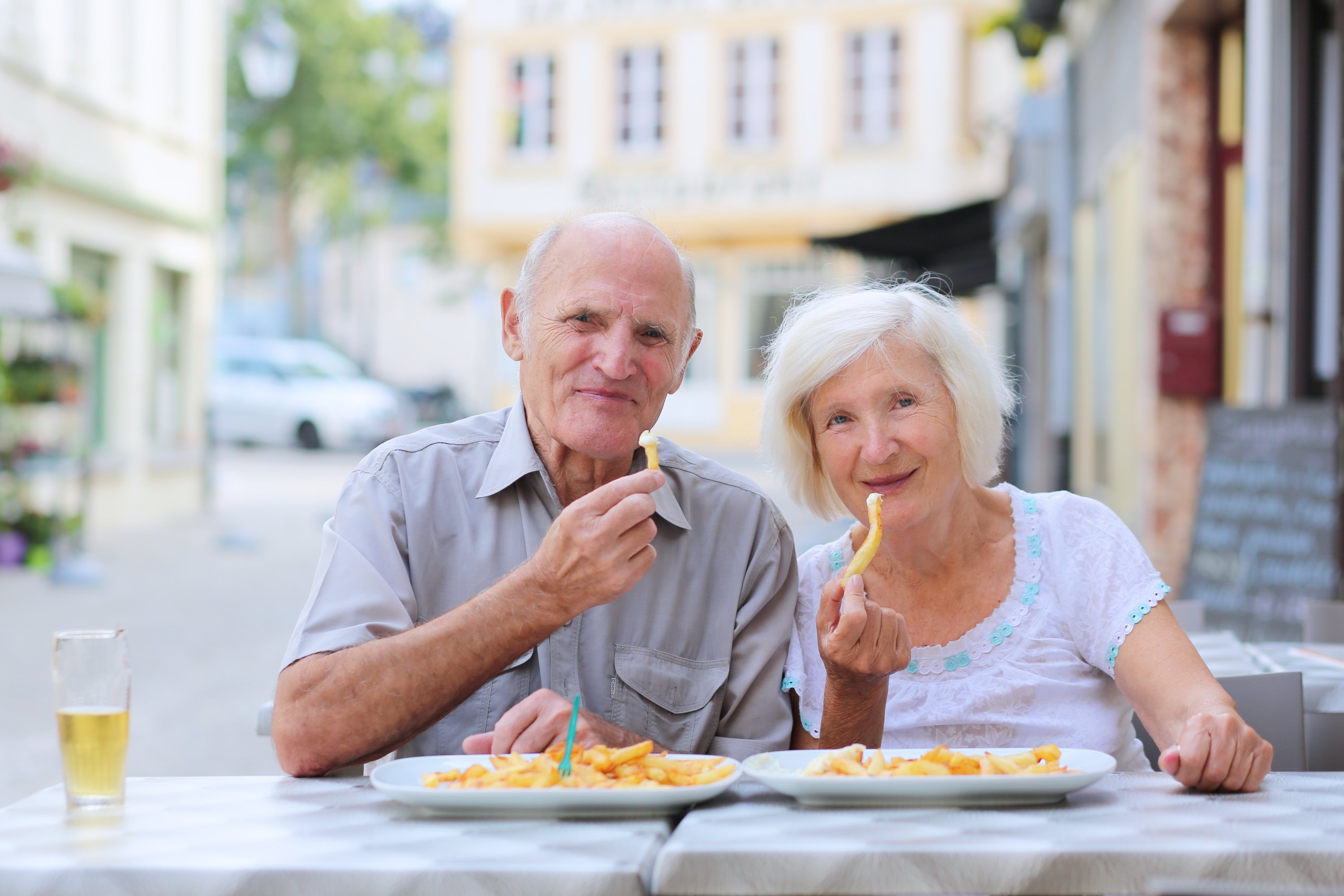 Happy active senior couple enjoying time together eating belgian french fries in outdoors street cafe on a summer day in typical European town | Photo: Shutterstock.com