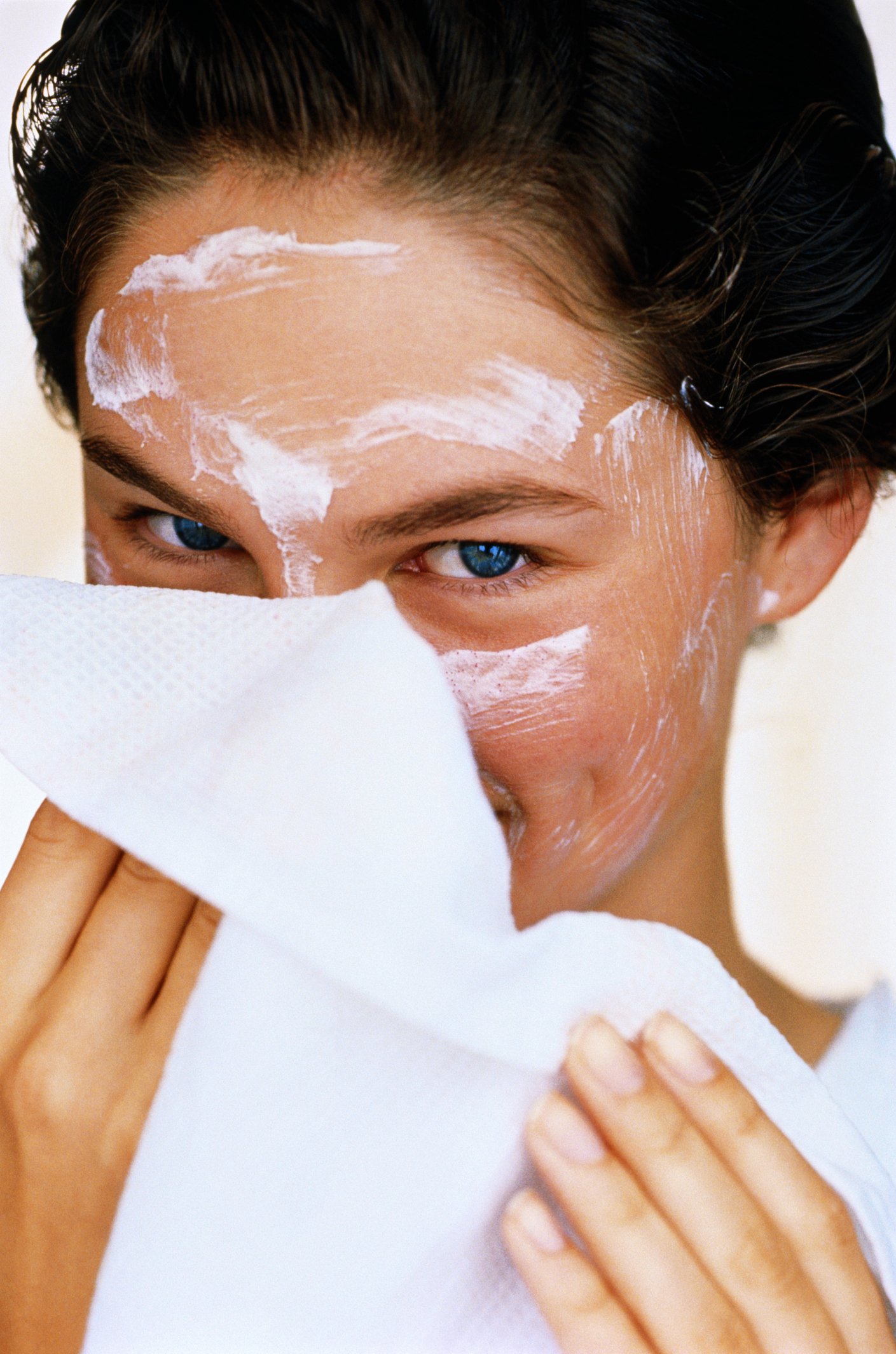 Photo d'une jeune femme essuyant une crème blanche sur son visage avec un tissu blanc | Source : Getty Images 