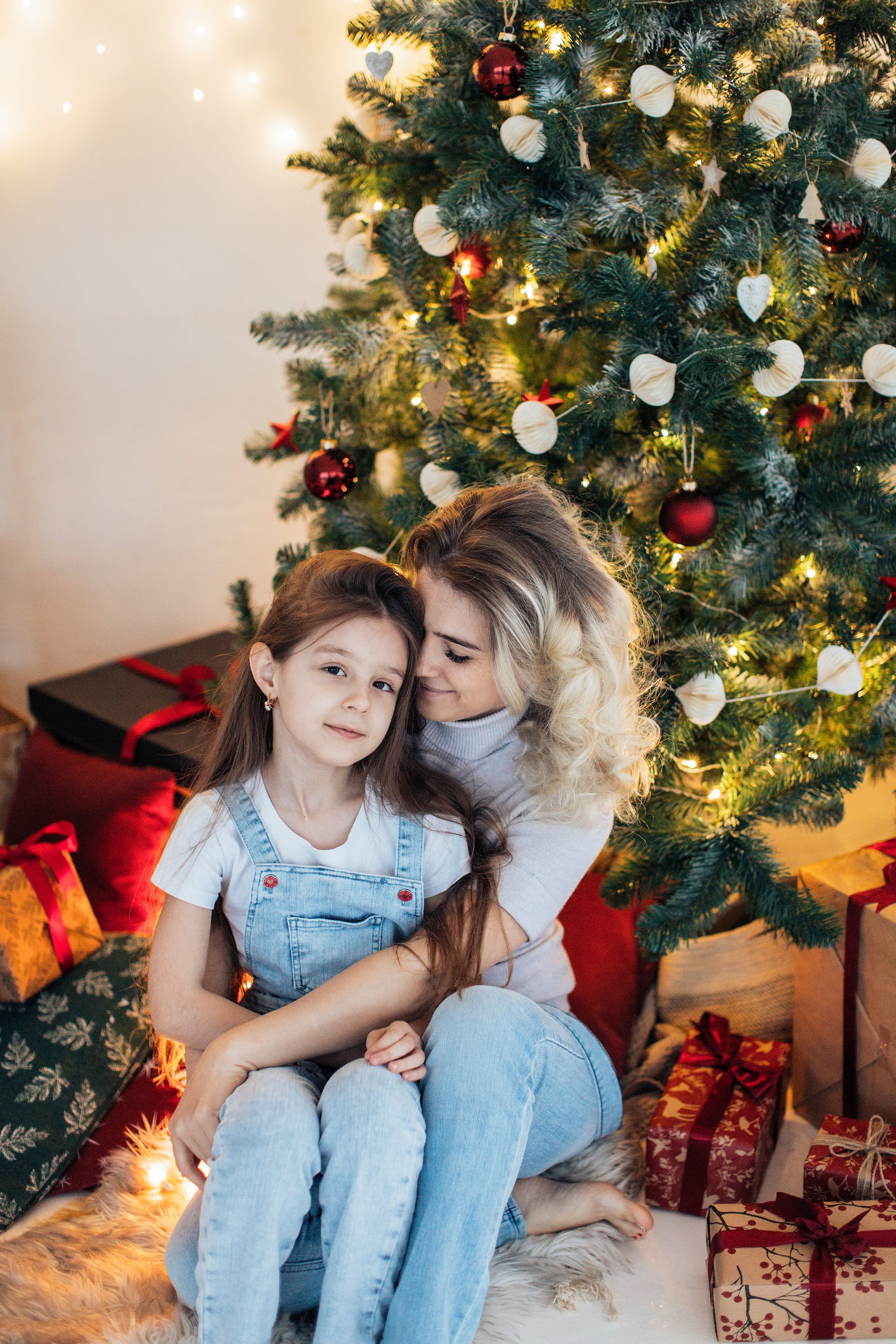 A mother hugging her daughter while sitting next to a Christmas tree | Source: Pexels