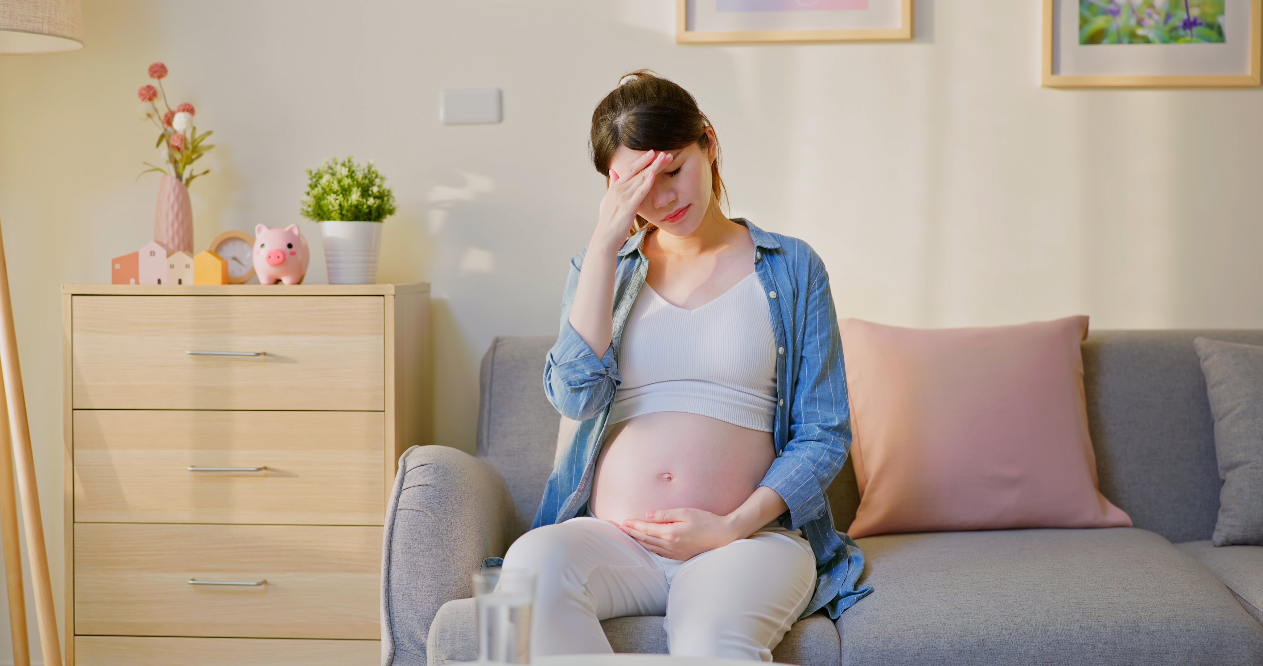 A pregnant woman sitting on a couch with her hand on her forehead | Source: Shutterstock