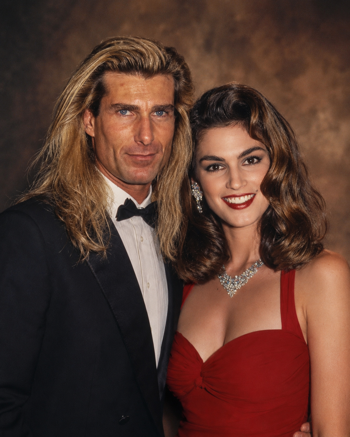 In an AI-generated formal portrait, Fabio stands beside Cindy Crawford as she strikes a pose in a classic red gown, capturing early 1990s high-fashion glamour. | Source: ChatGPT