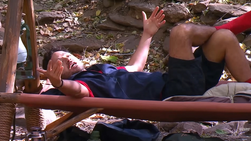 Adam Thomas throws his arms up in exasperation while lying in camp, capturing a moment of visible frustration during the tense exchange. | Source: YouTube/I'm A Celebrity... Get Me Out Of Here!