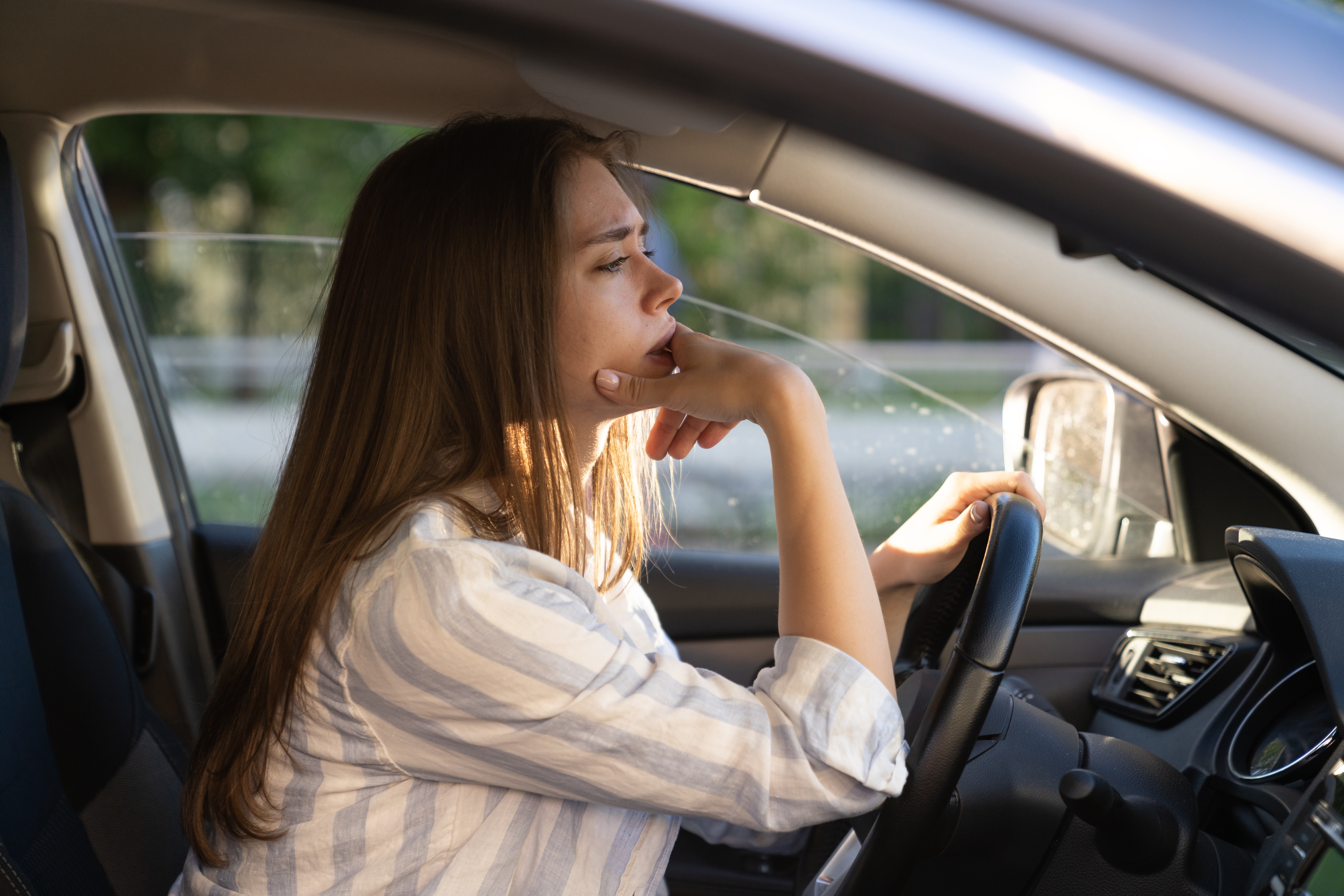 Unhappy female driver depressed and anxious hold hand on steering wheel look at road with anxiety. | Source: Shutterstock
